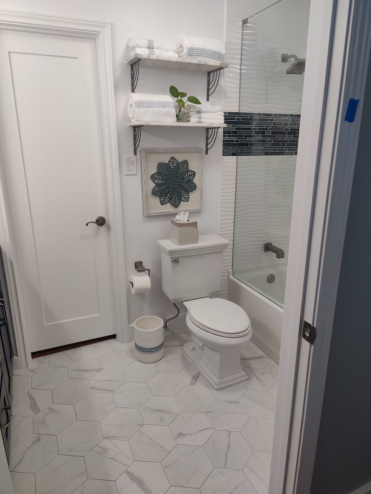 White bathroom with toilet, shelves, and shower. Marble tile flooring.
