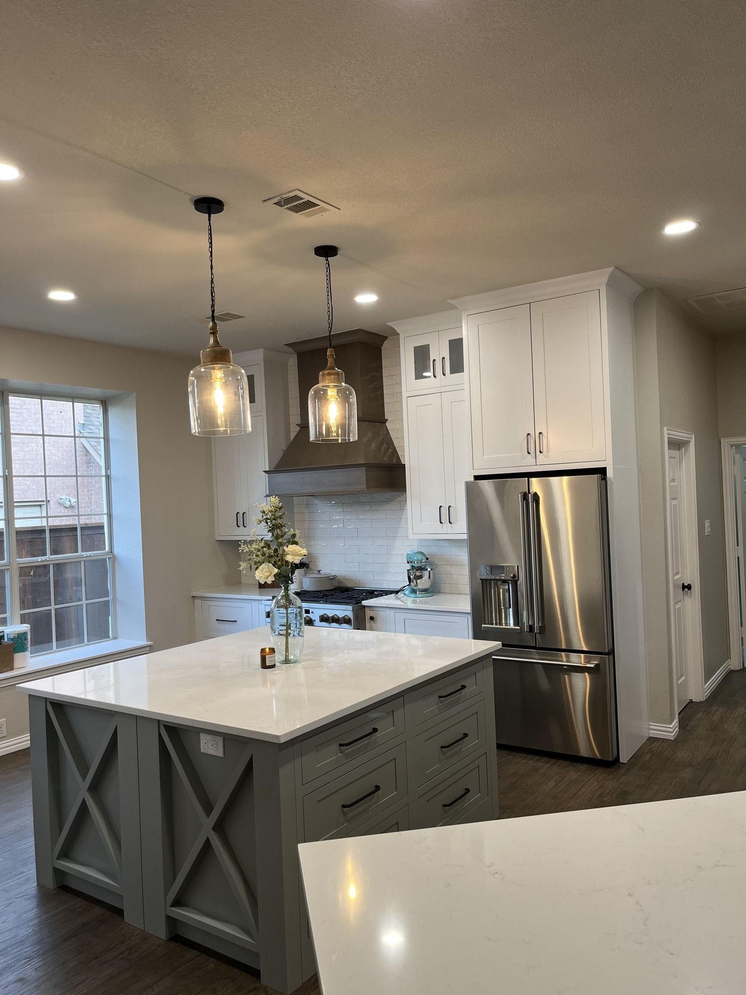 Kitchen with gray and white cabinets, island, stainless steel refrigerator, and pendant lights.