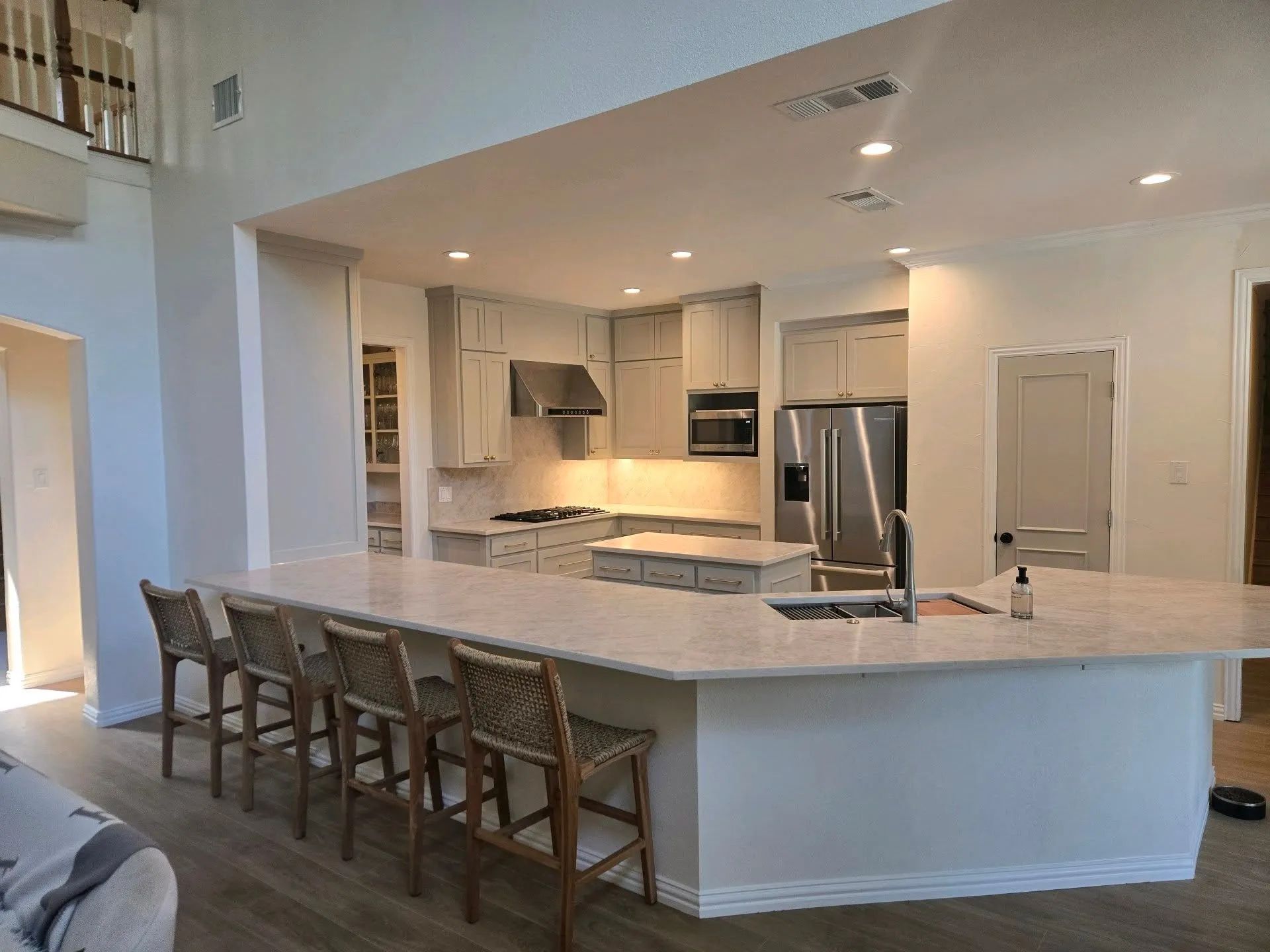 Bright modern kitchen with white island, bar stools, stainless appliances, and recessed lighting
