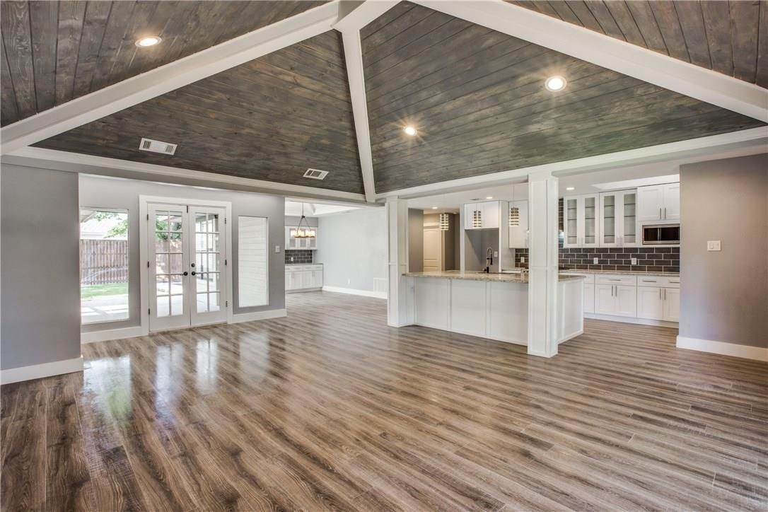 Open-plan home interior featuring high vaulted wooden ceilings, light wood-style flooring, and a kitchen with white cabinets.