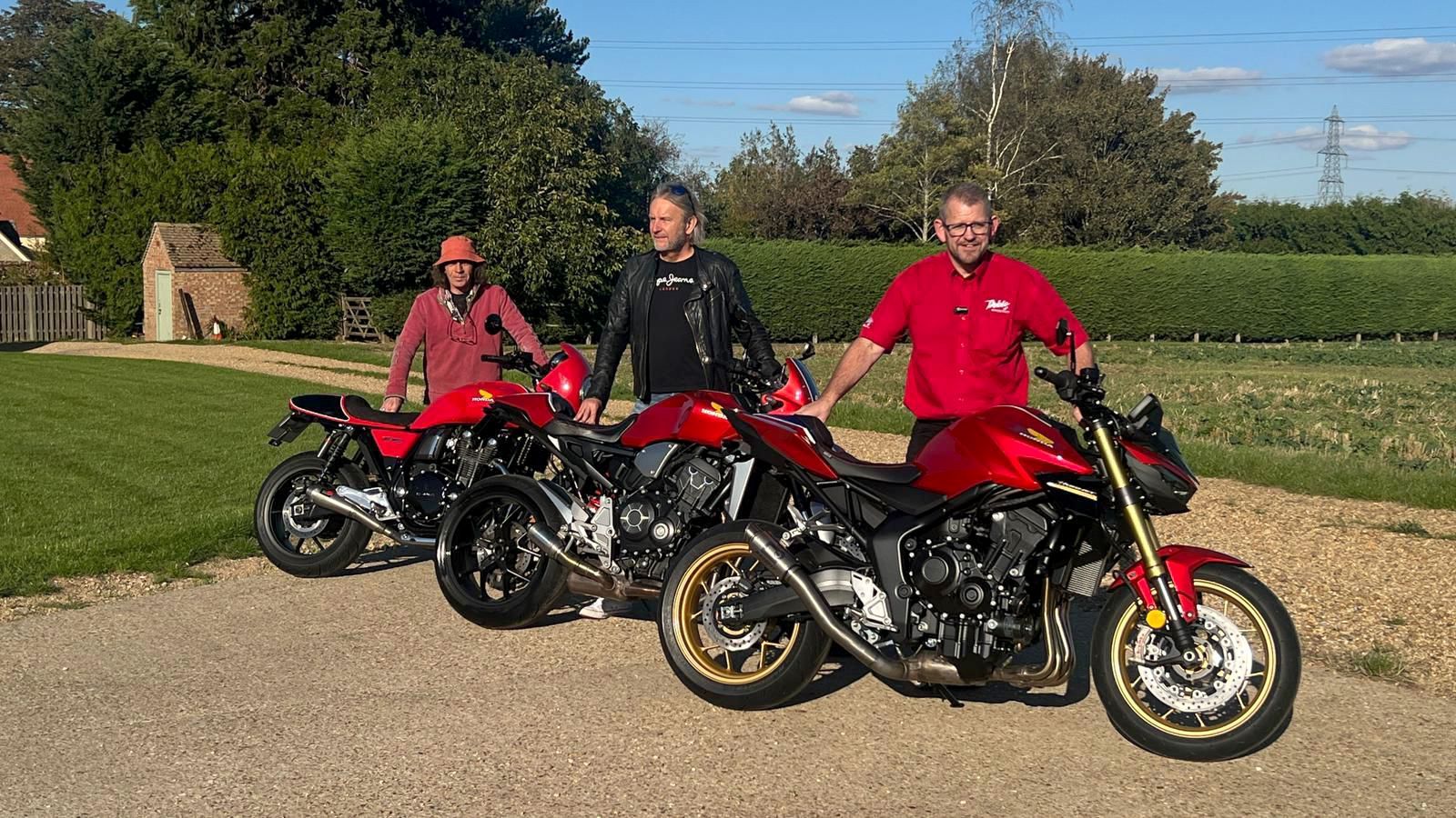 Three men with red motorcycles parked outdoors.
