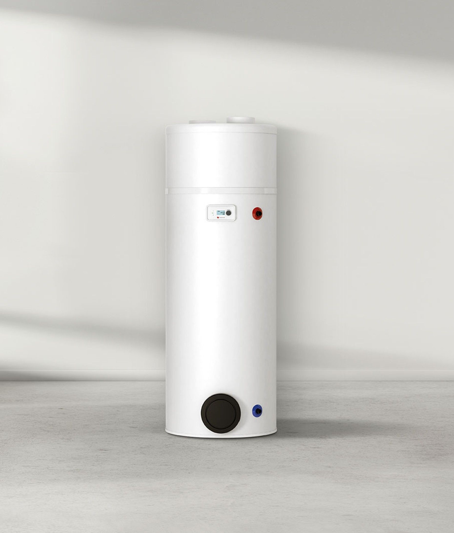 Appareil cylindrique blanc sur un sol gris, adossé à un mur uni, avec un cadran noir et de petits indicateurs rouges et bleus.