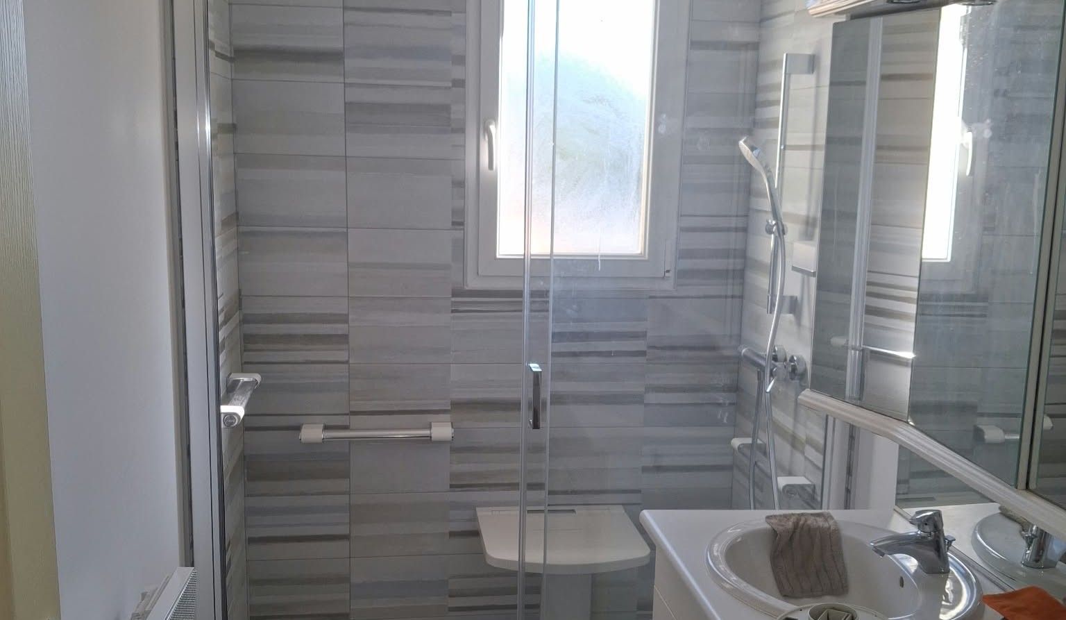Salle de bain après rénovation par RPCE : douche à l'italienne avec paroi vitrée, carrelage gris et double vasque