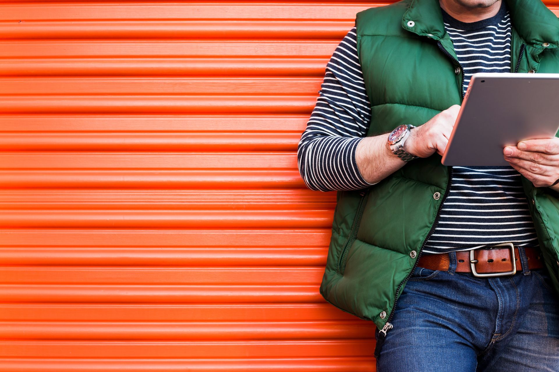  
[Alt Image Tag: Man checking tablet outside orange roll-up door for self storage solutions
