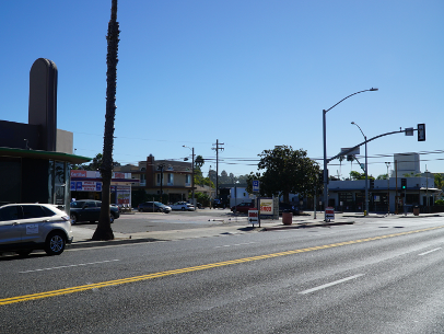 Sunny street intersection with cars, traffic lights, palm trees, and storefronts in the distance