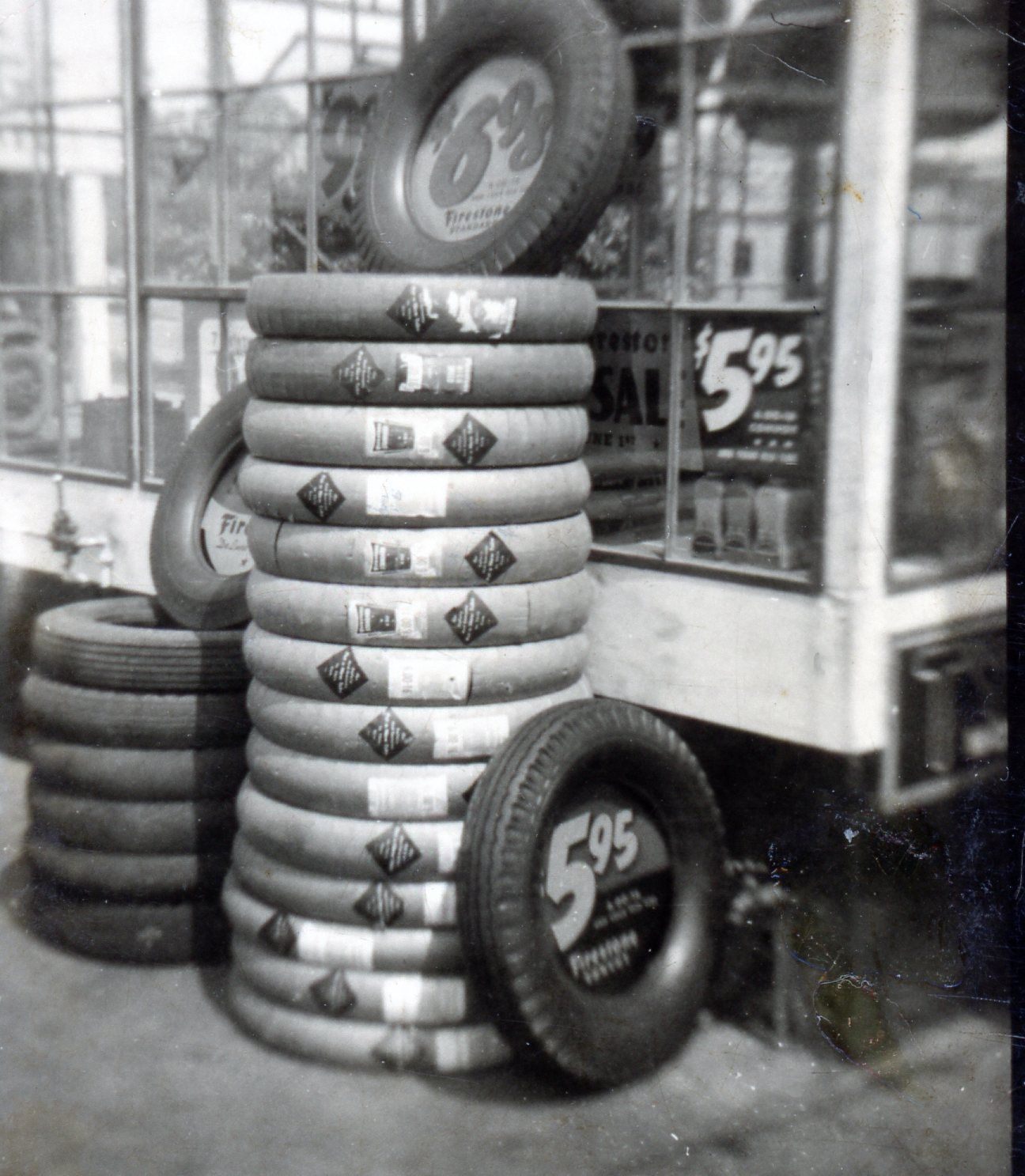 Stacked tires displayed outside a shop window with a price sign reading $5.95