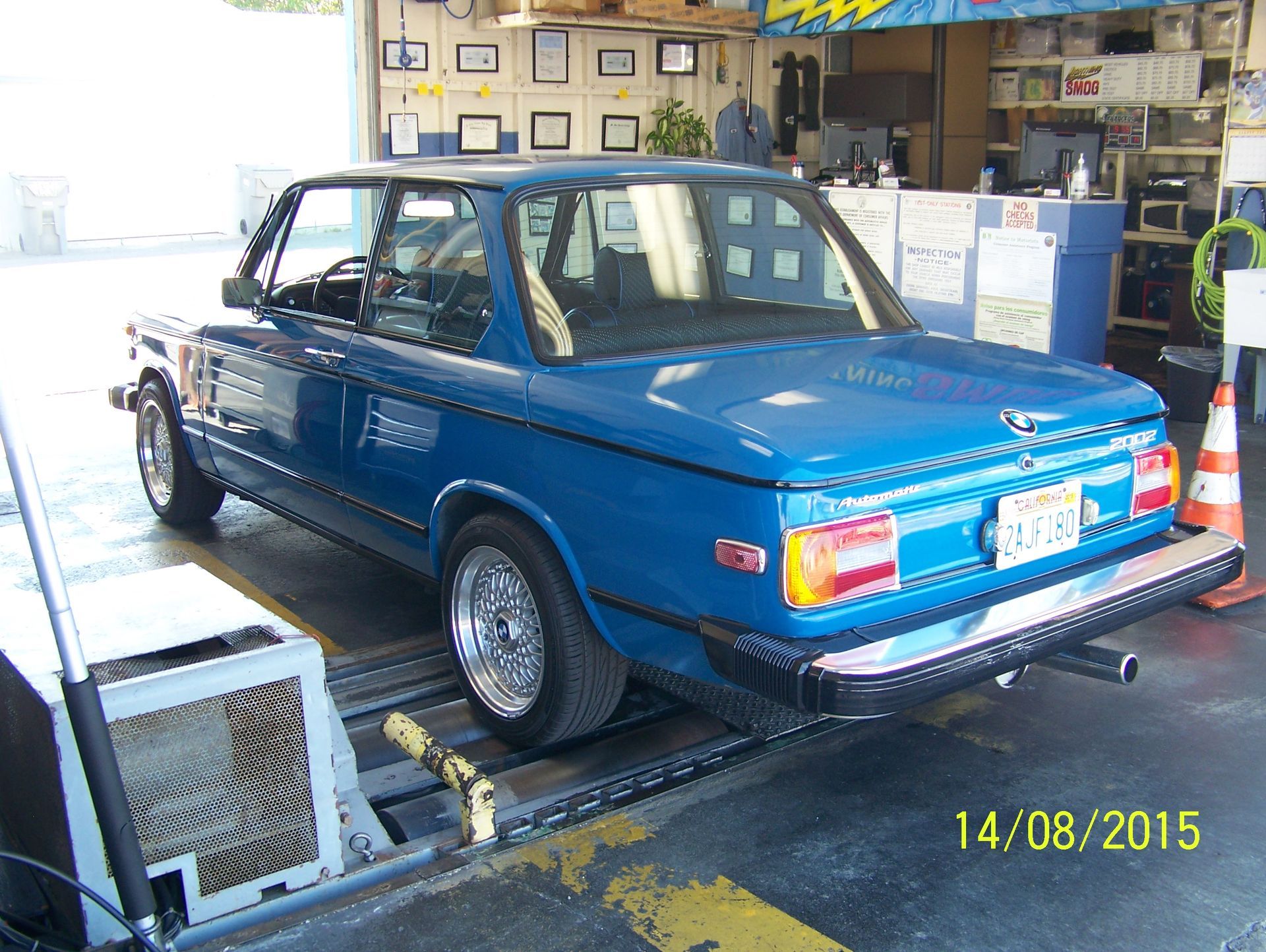Blue vintage sedan on a dynamometer in a workshop, with equipment and tools around it.