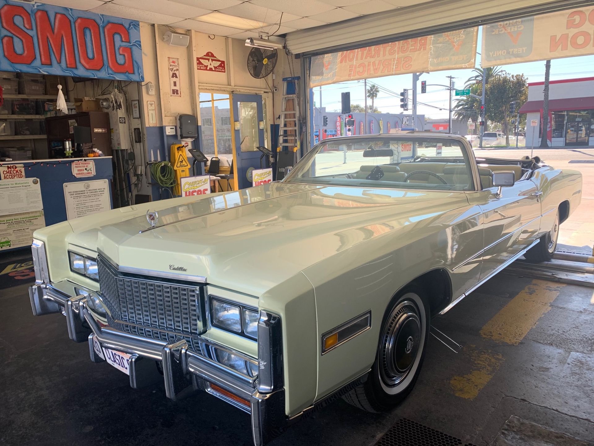 Vintage white convertible in a garage, parked near a SMOG sign and service equipment.