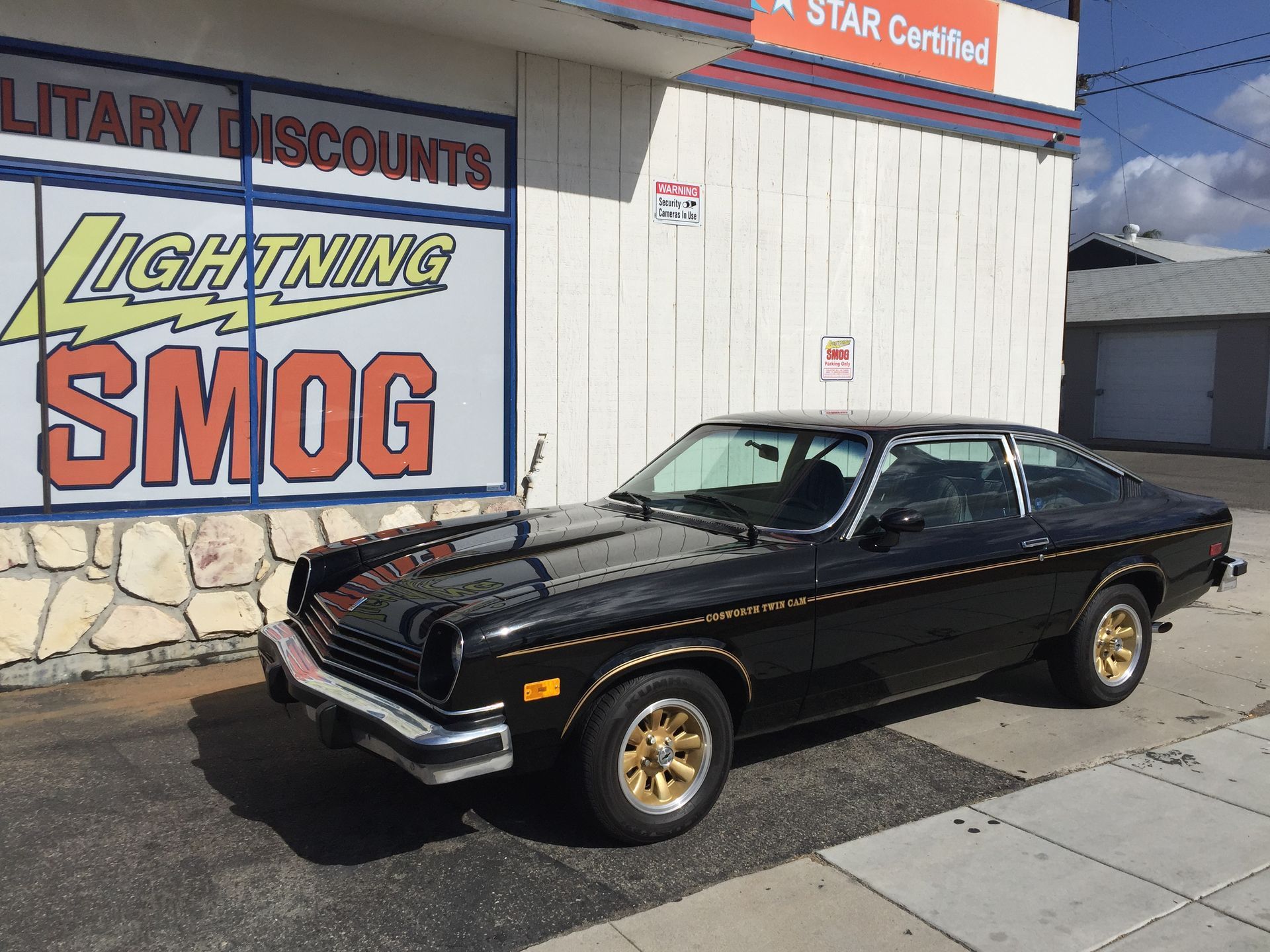 Black classic coupe parked outside a Lightning Smog shop on a sunny sidewalk