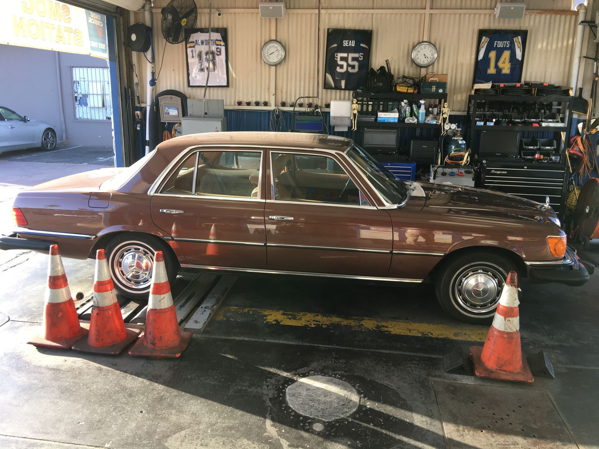Maroon classic car parked in a garage with orange traffic cones in front