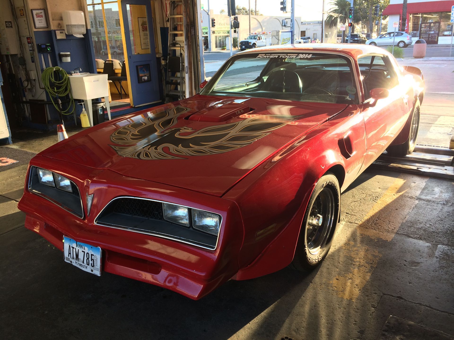Red classic sports car parked at a gas station, viewed from the front left.