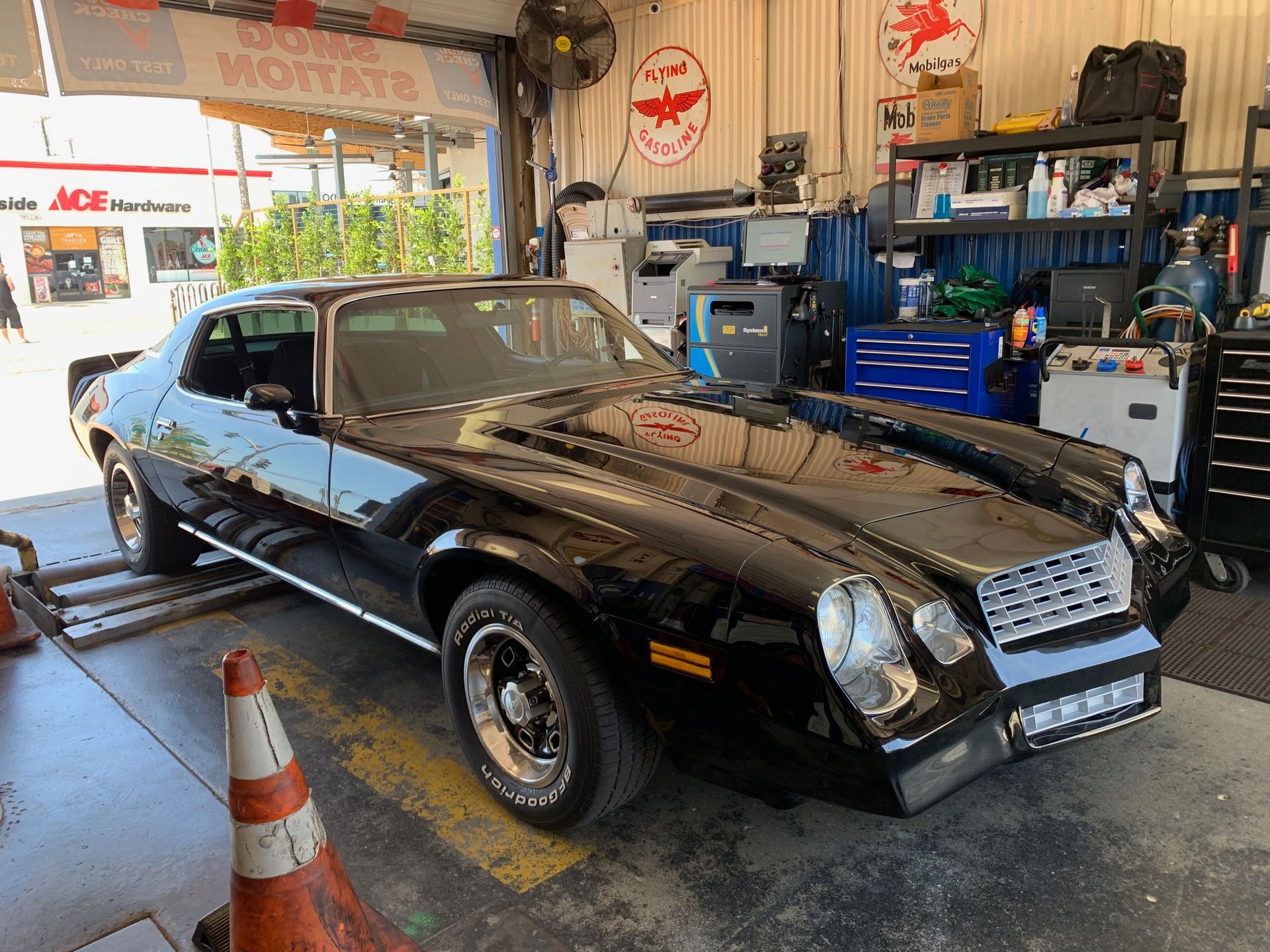 Black classic muscle car in an auto shop, parked under bright lights with tools and equipment nearby