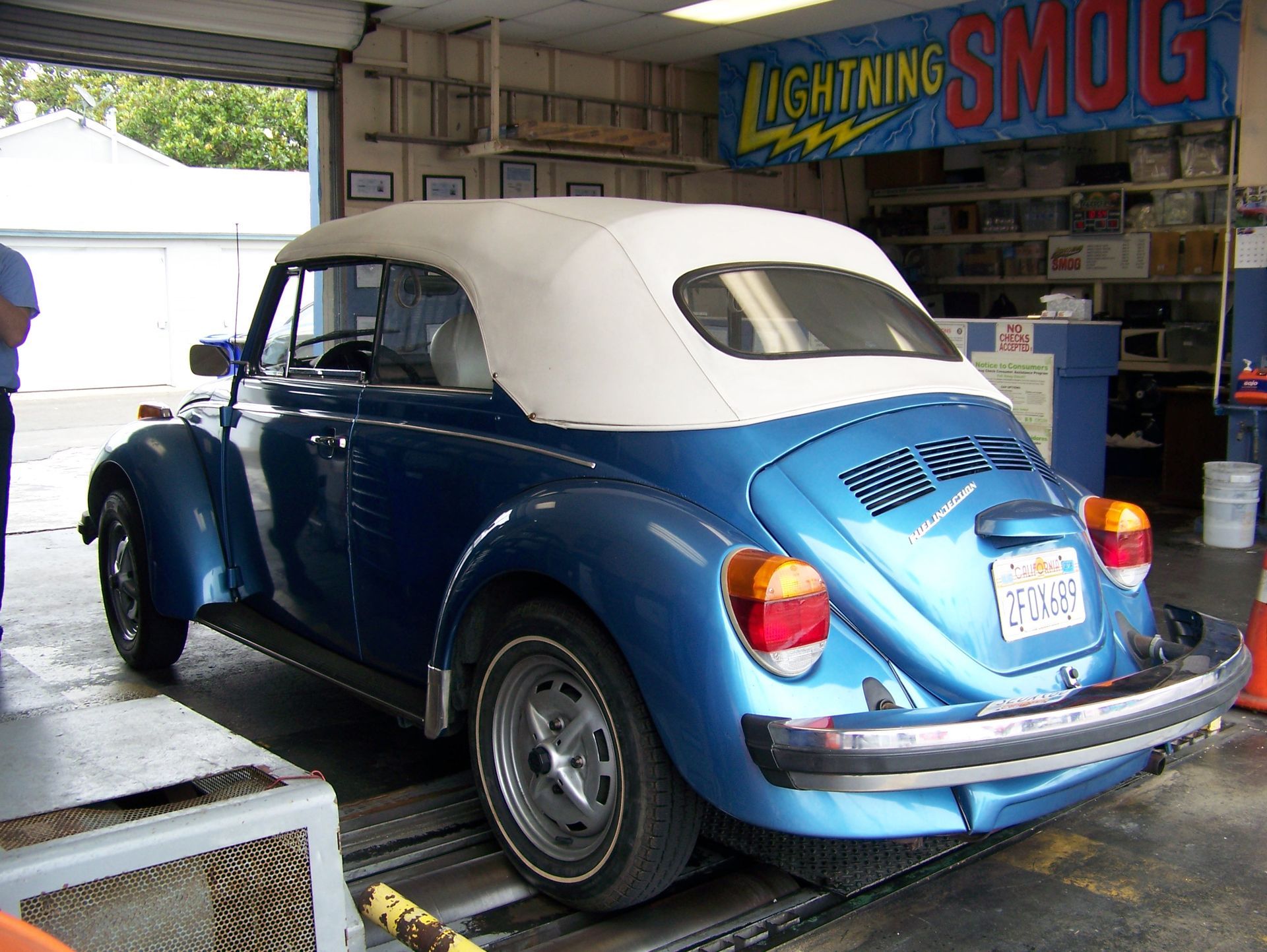 Blue vintage Volkswagen Beetle in a garage, viewed from the rear with a white soft top.