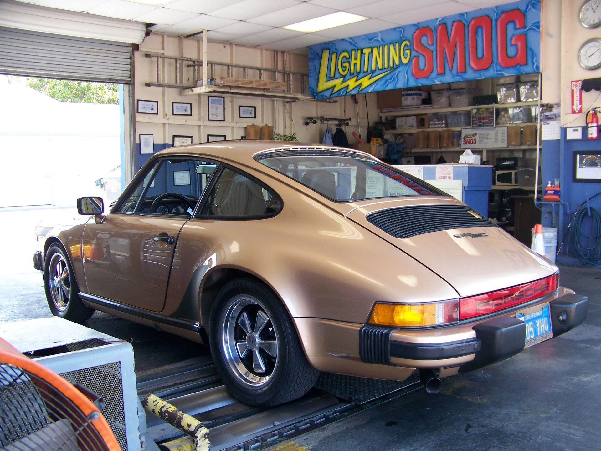 Gold classic Porsche in a smog shop garage with a Lightning Smog sign overhead