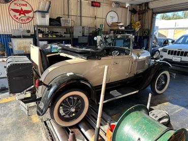 Vintage beige-and-black convertible in an auto shop, with tools and equipment around it.