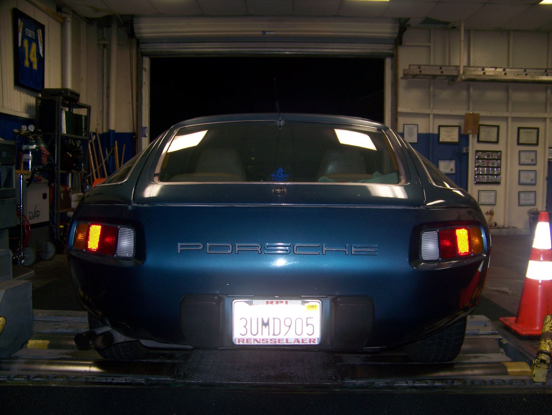 Blue Porsche rear in an auto shop bay with brake lights on and cones nearby