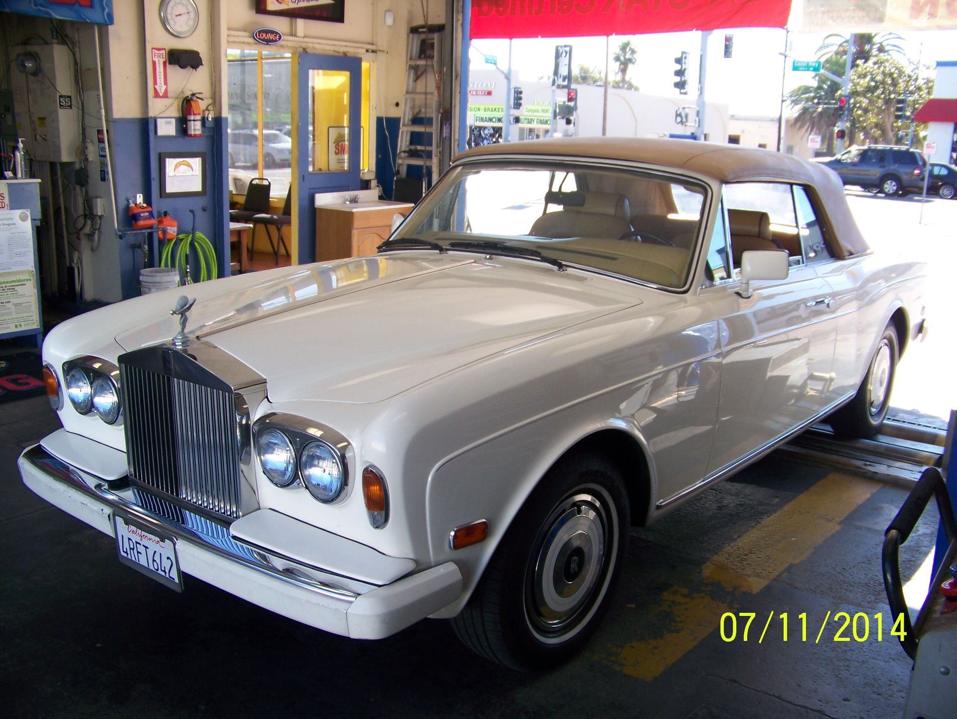 Silver Rolls-Royce parked indoors at a service bay, front view with yellow date stamp