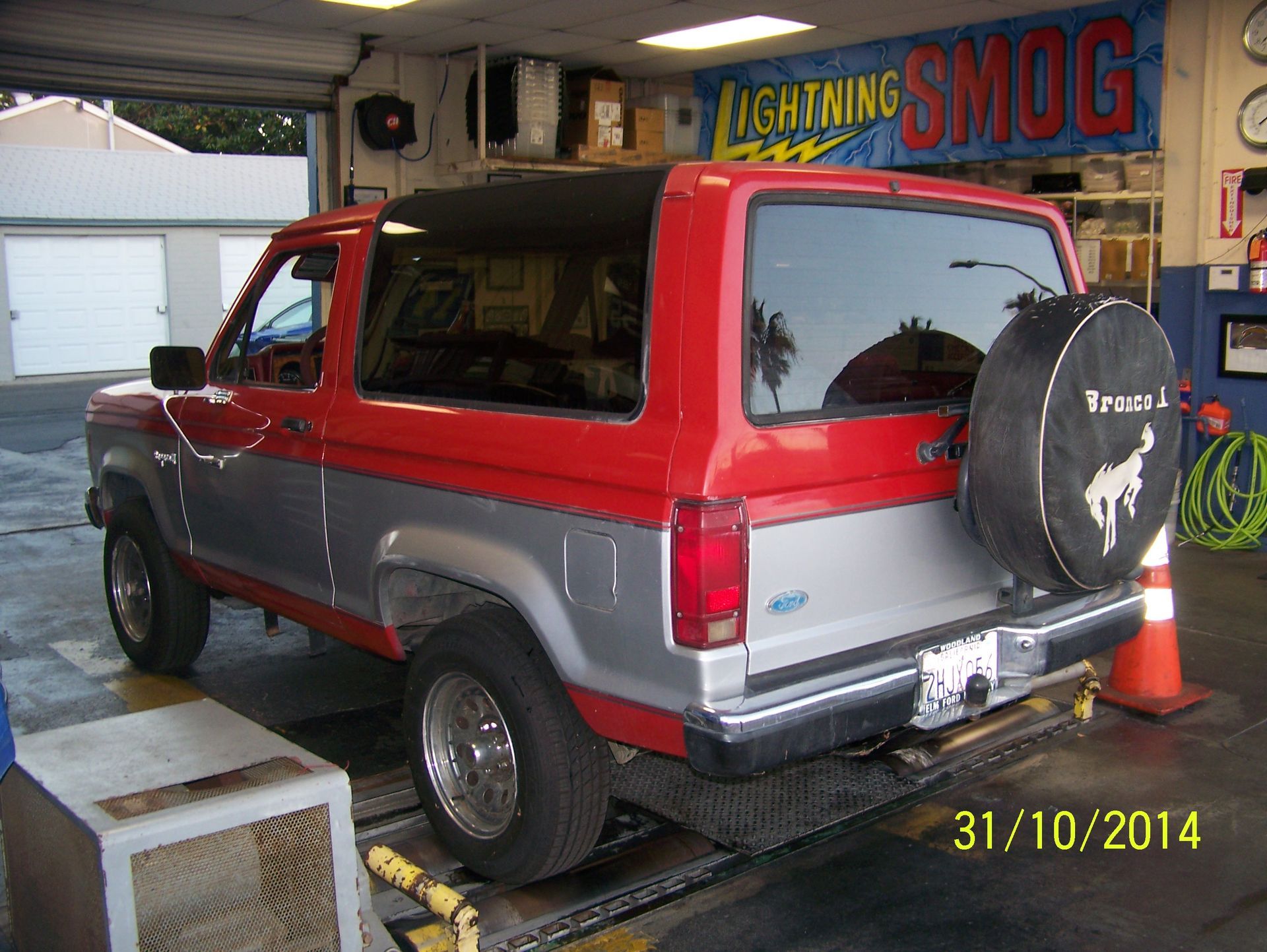 Red SUV at an auto shop with hood open, near a smog test sign and cones
