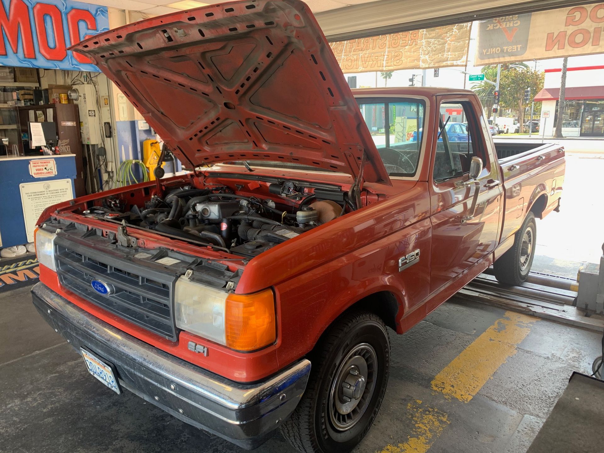 Red pickup truck in a garage with the hood open for inspection.