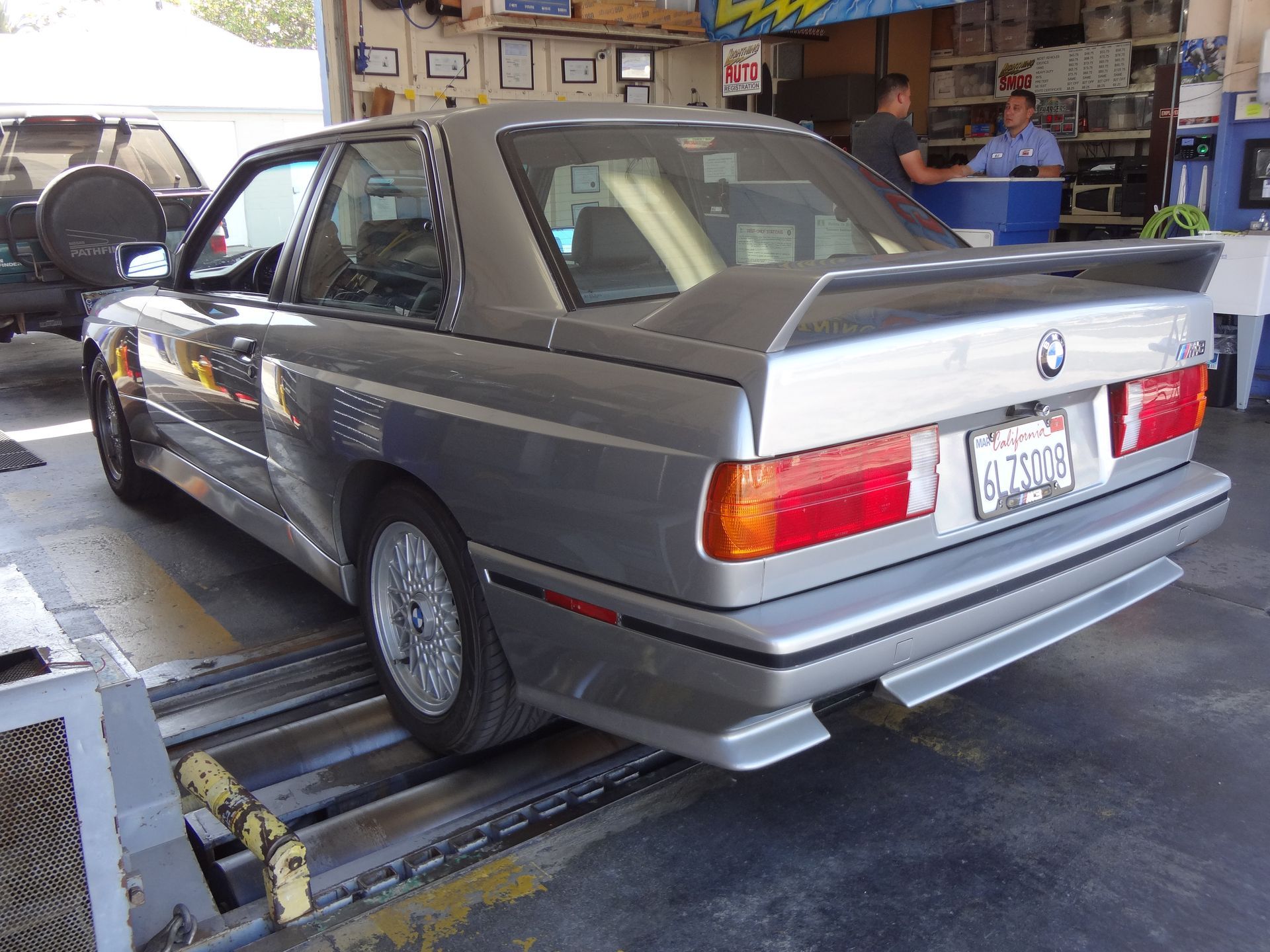 Gray BMW sedan on a car lift in an auto repair garage, rear view.