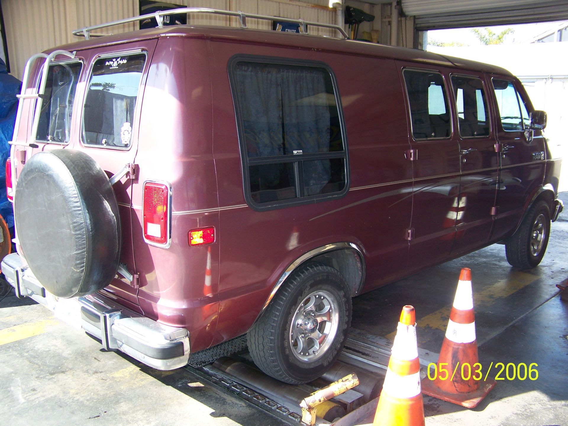 Maroon van parked in a garage, rear spare tire visible, with traffic cones nearby.