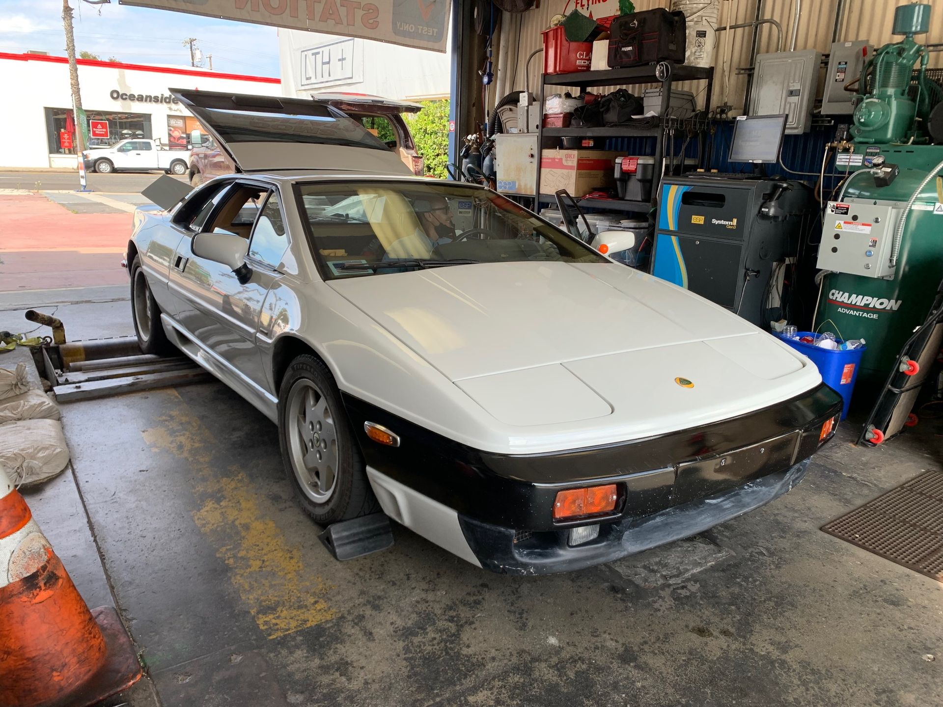 White sports car inside an auto shop, with hood open and rear hatch raised.