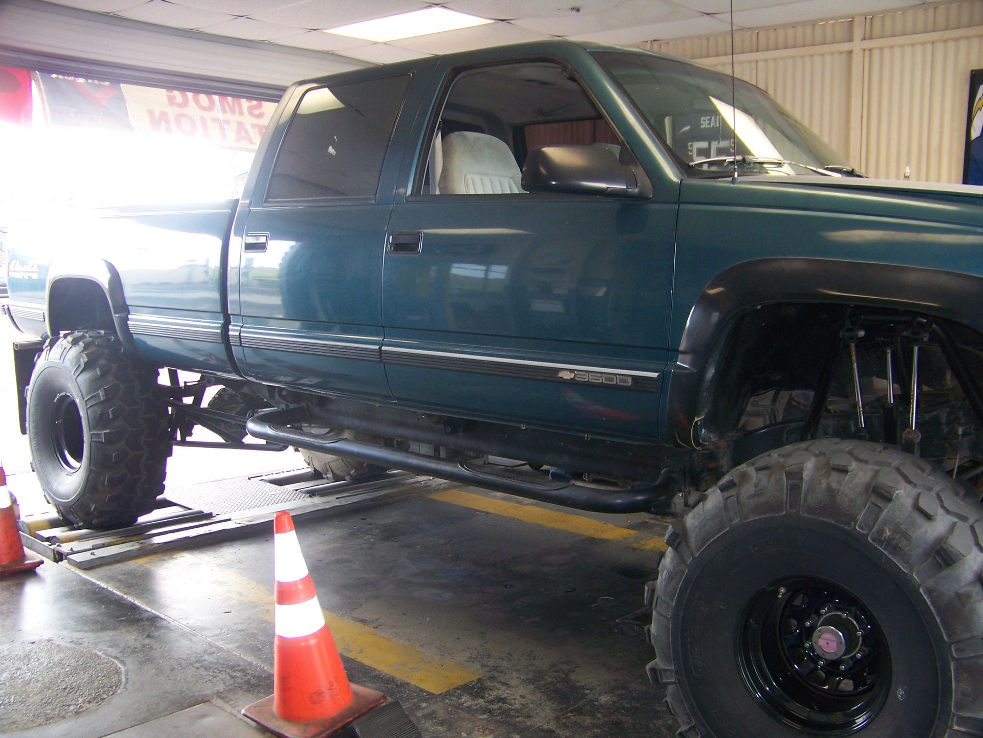 Lifted dark green pickup truck inside a garage with orange traffic cones nearby