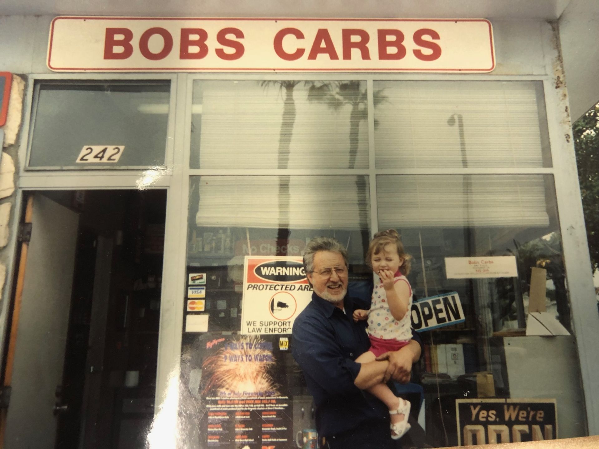 Man holding a child outside Bobs Carbs storefront with open sign and large front windows
