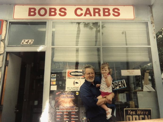 Man holding a child outside Bobs Carbs storefront with open sign and large front windows