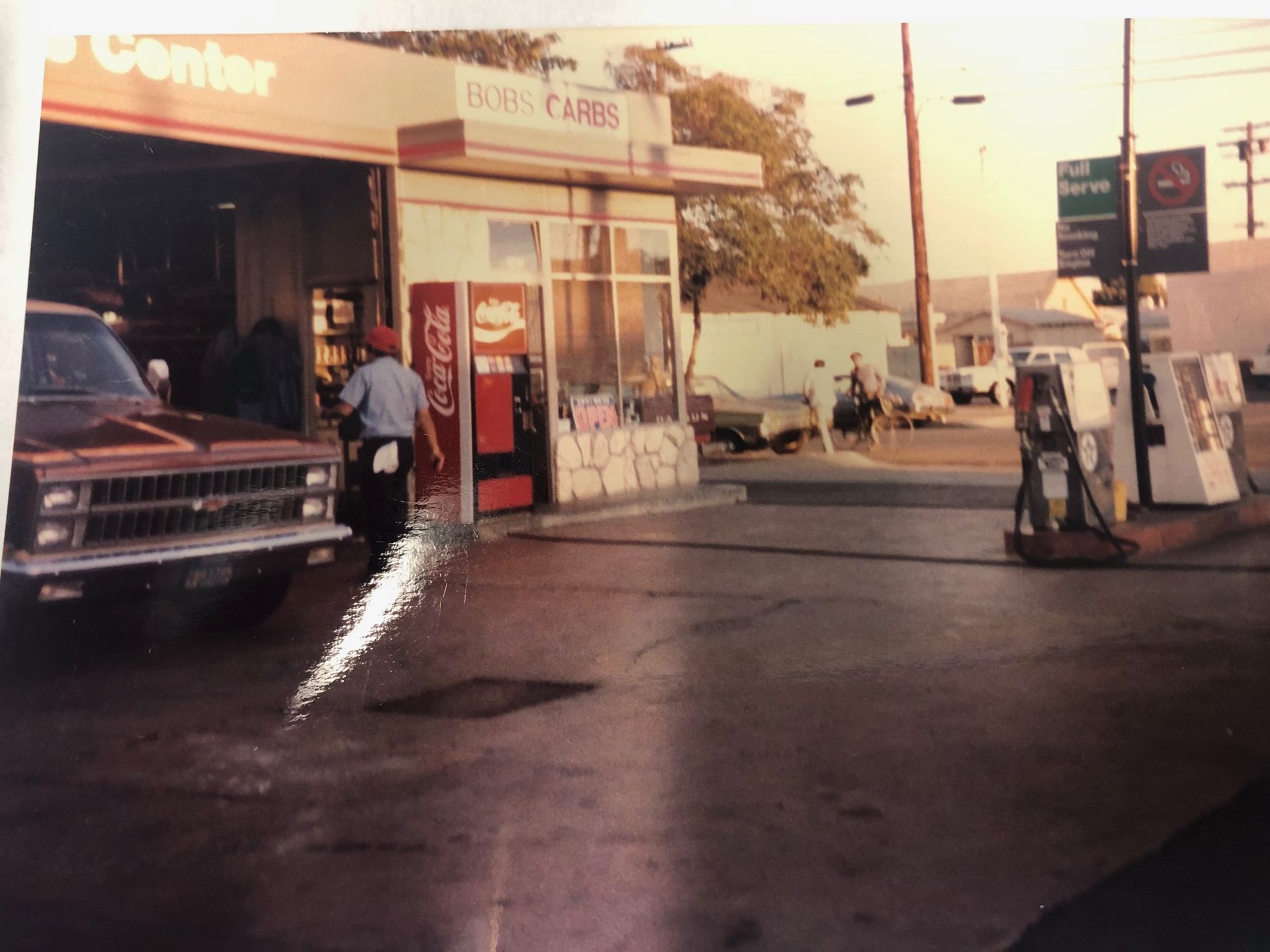 Gas station forecourt at dusk with a pickup truck, fuel pumps, and a person by the store entrance