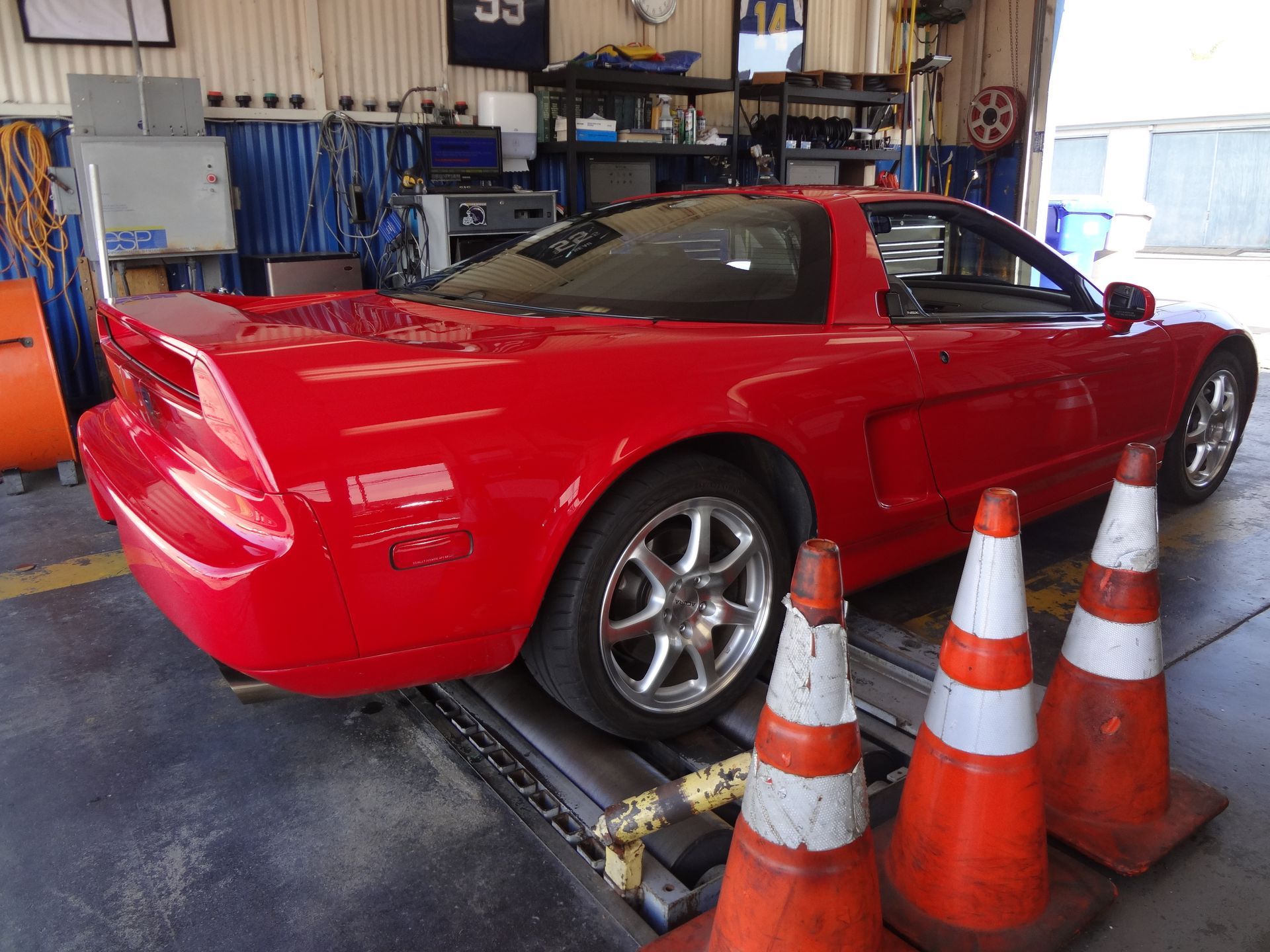 Red sports car on a shop lift in a garage, with traffic cones in the foreground.