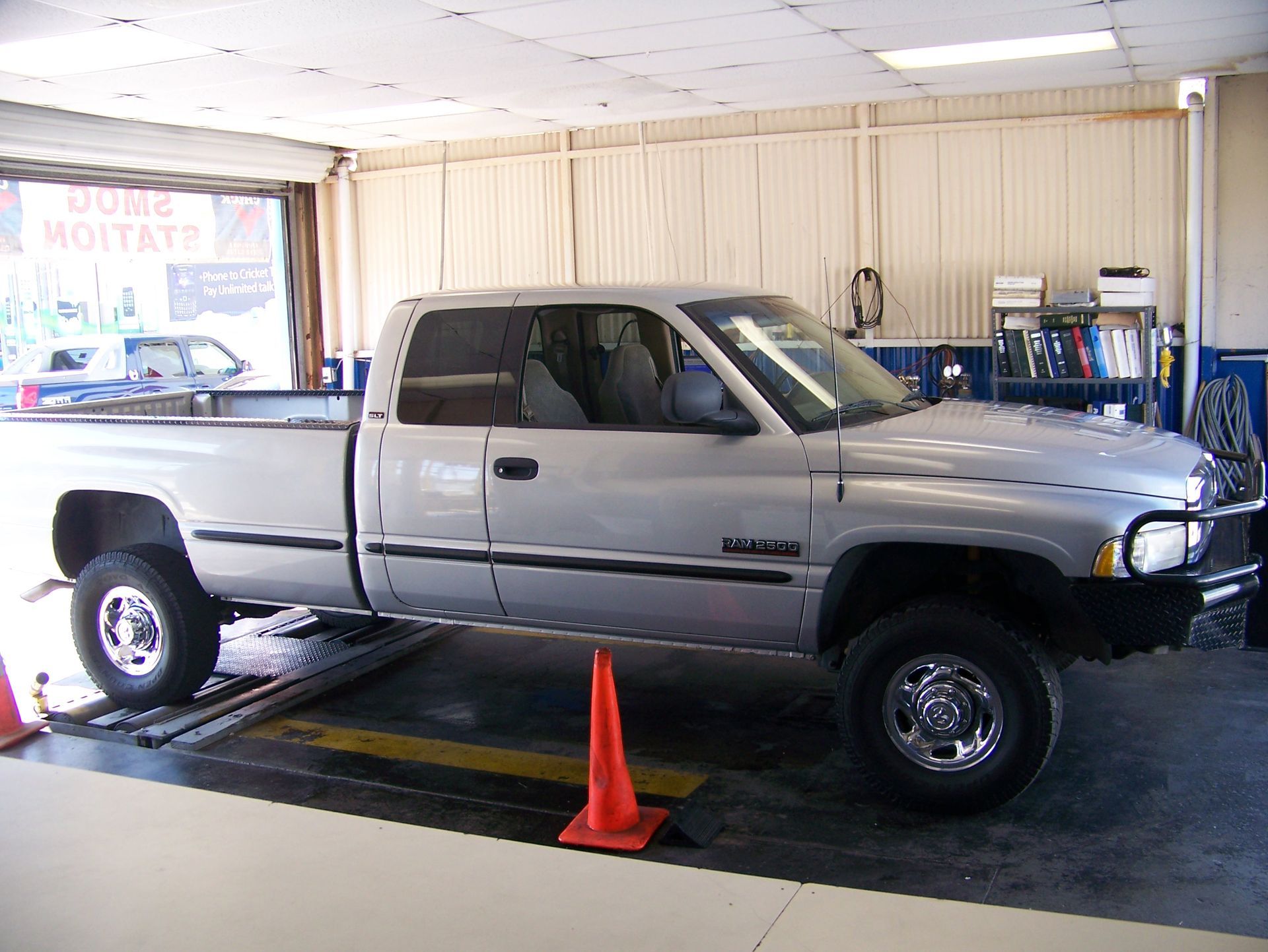 Silver pickup truck on a dyno in a garage, with an orange cone in front.