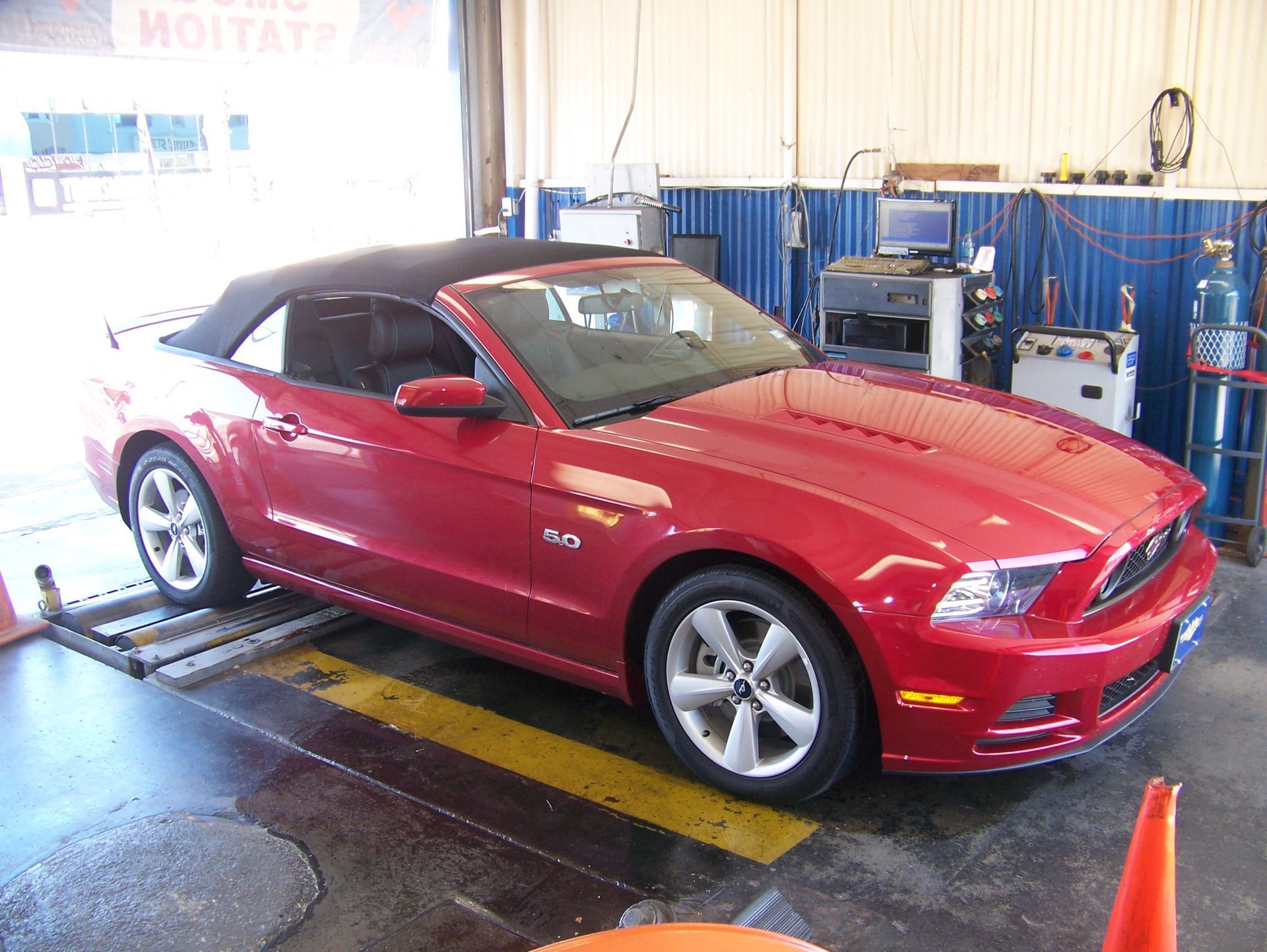 Red Ford Mustang on a shop lift inside an auto service garage