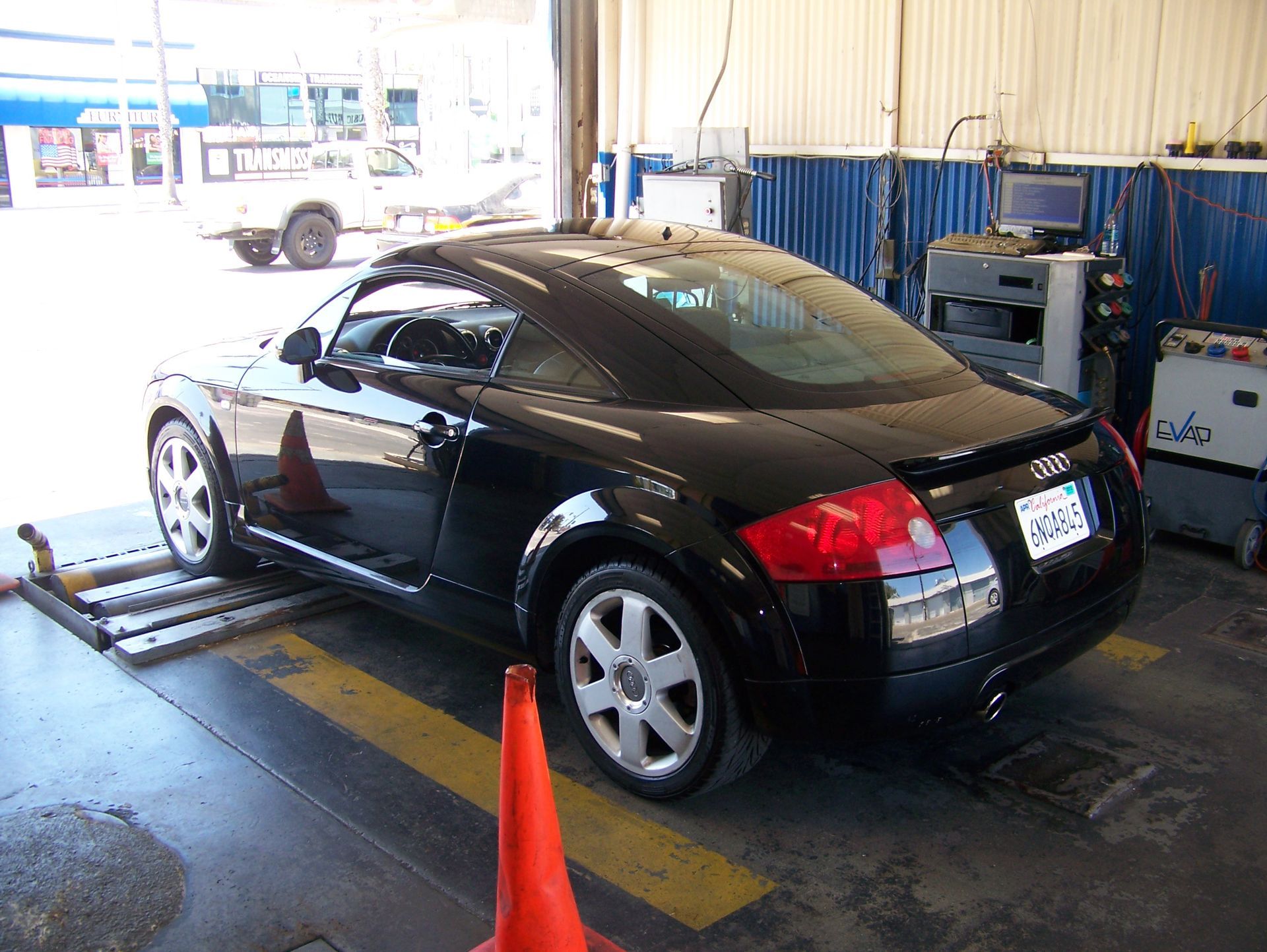 Black sports coupe in an auto shop on a lift, with orange cone in front of it.