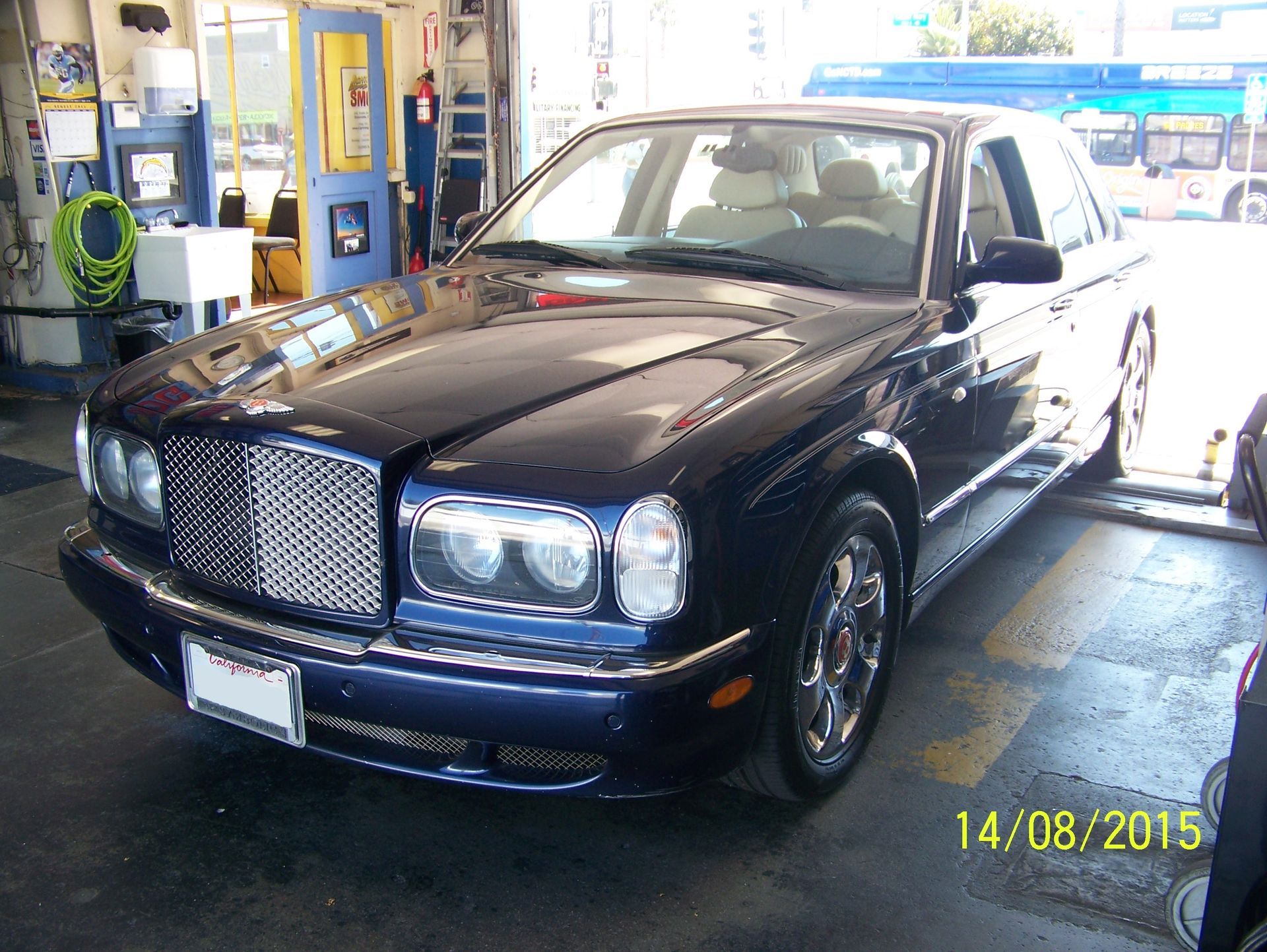 Black luxury sedan at a gas station, parked near a pump with a yellow date stamp.