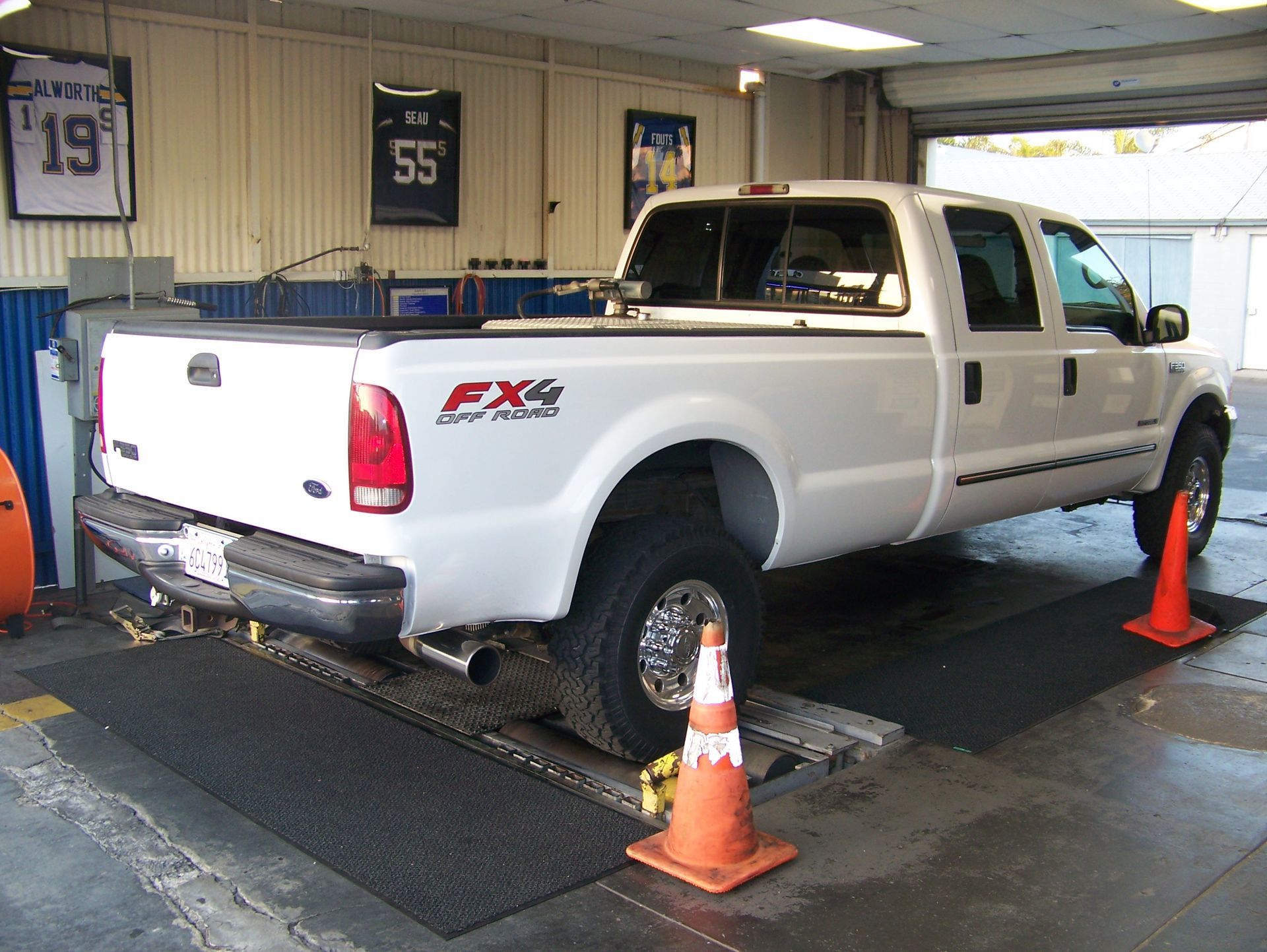 White Ford pickup truck on a dynamometer inside an auto shop, secured by orange cones and straps