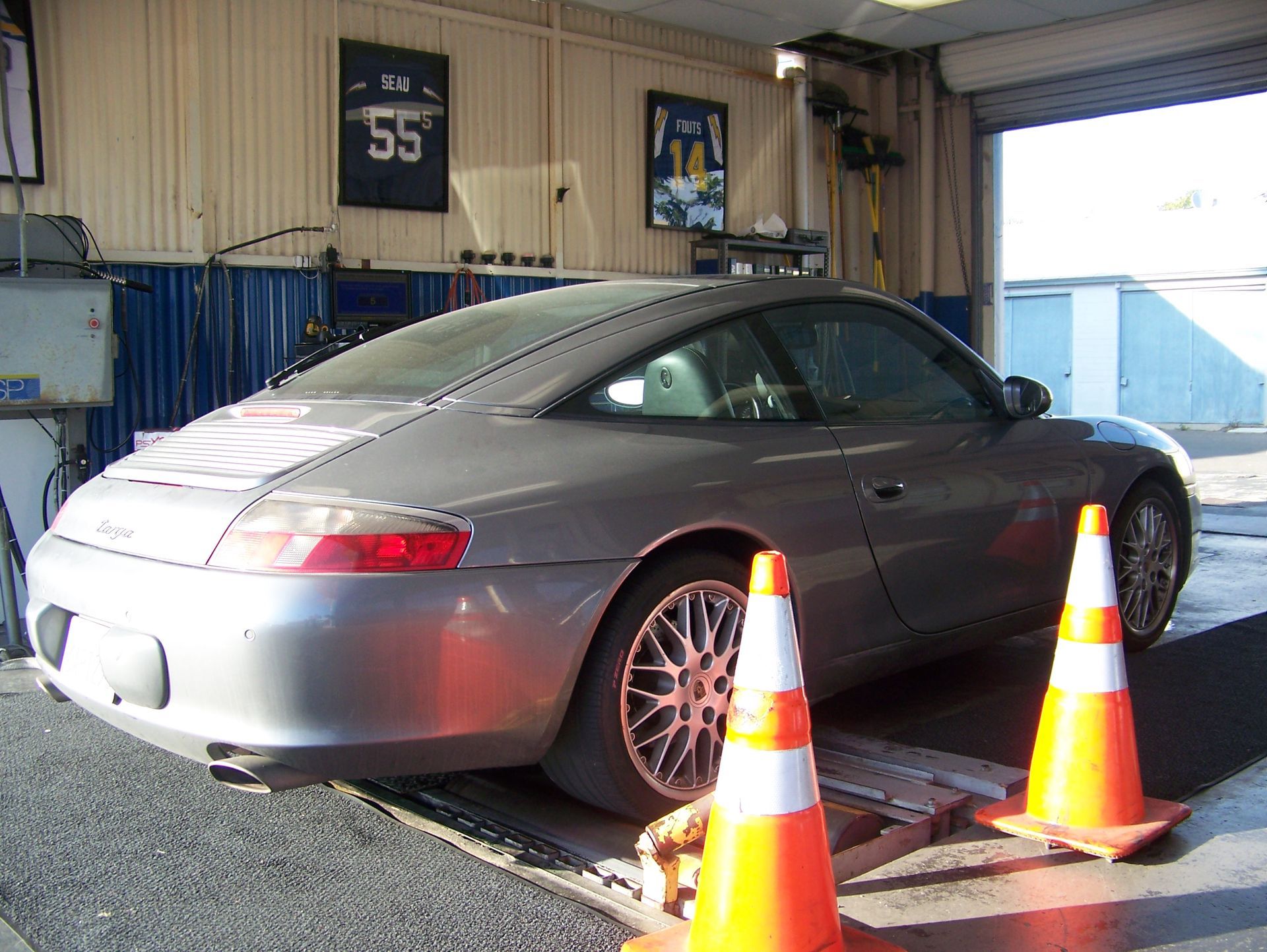 Gray sports car on a dynamometer in a garage, with orange traffic cones in front.