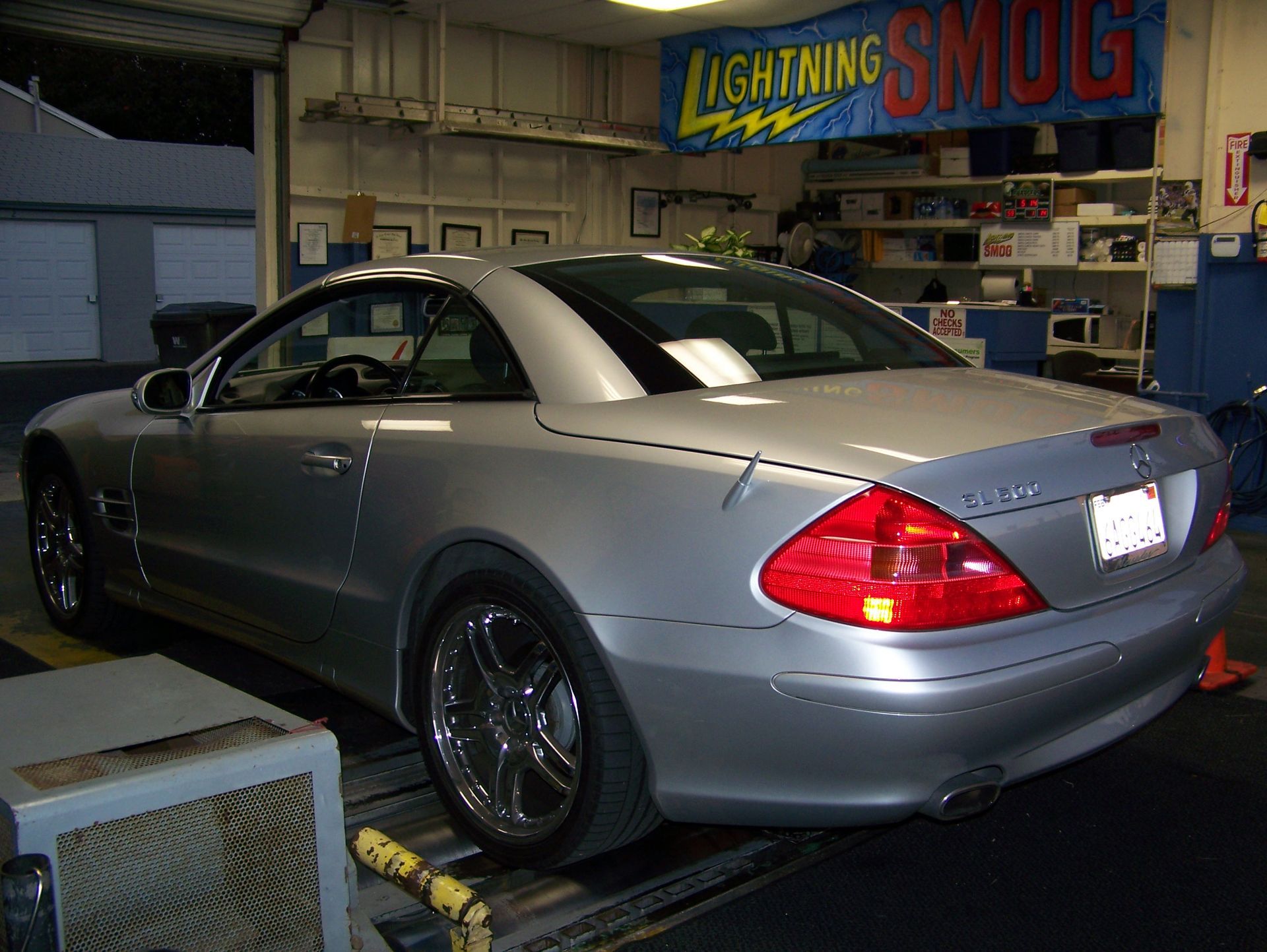 Silver sports coupe parked inside an auto shop with a Lighting and SMOG sign in the background