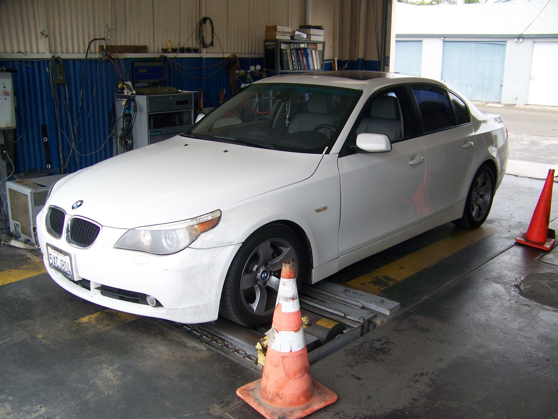 White sedan in an auto shop, parked on a lift with orange cones around it