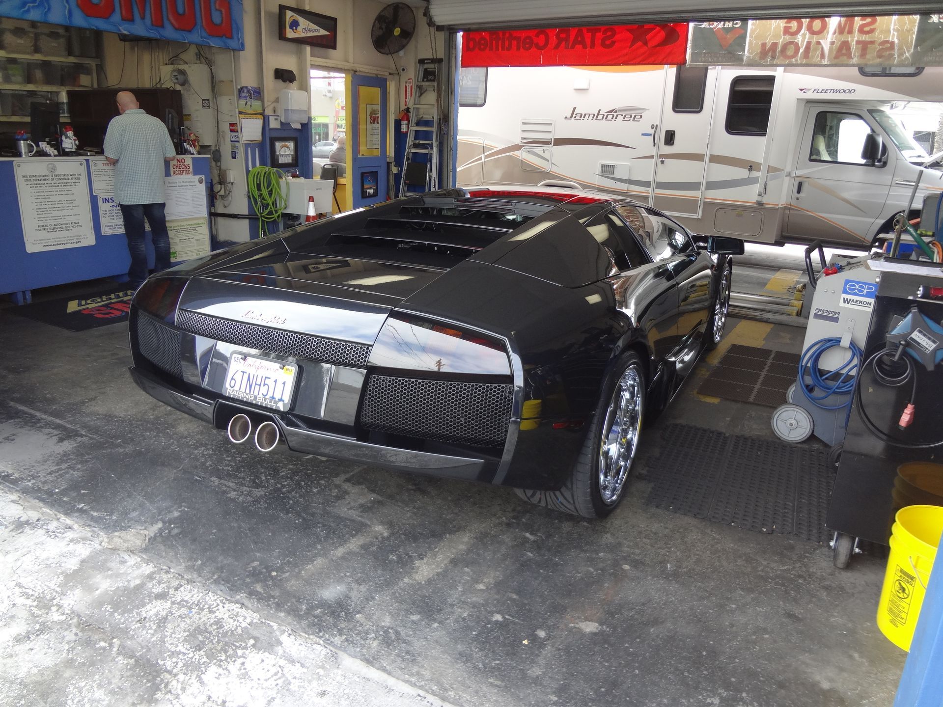 Black sports car in an auto shop garage with a mechanic working nearby