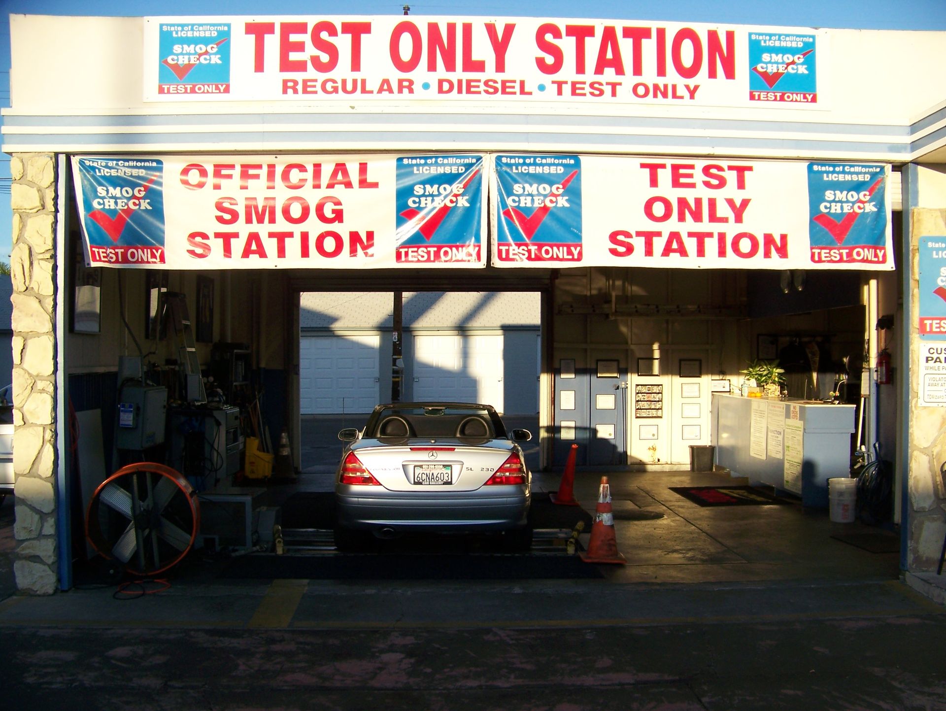 Car at an official smog test station with red and blue signs, viewed from the open service bay