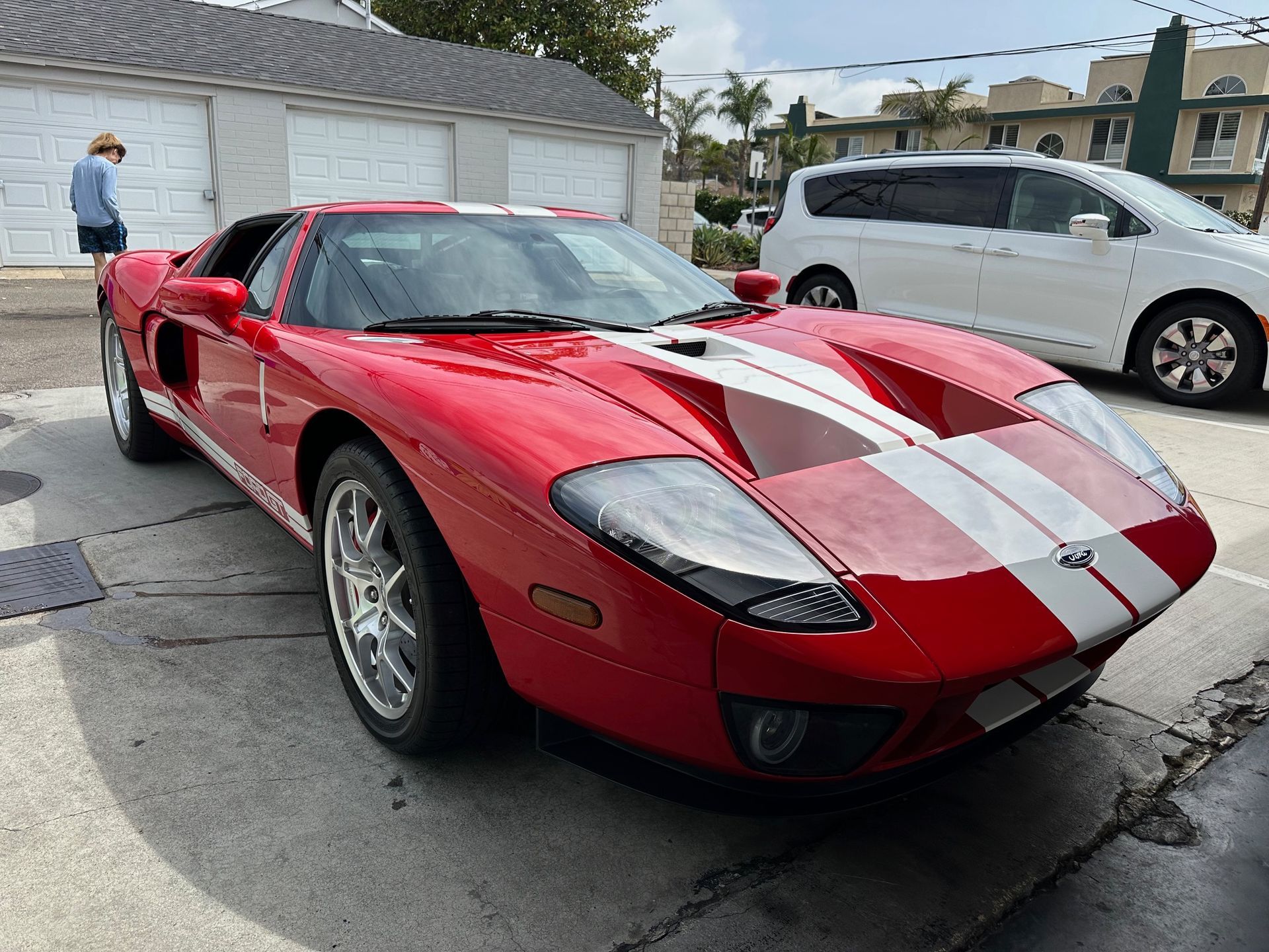 Red Ford GT sports car with white racing stripes parked in a driveway with a person nearby.
