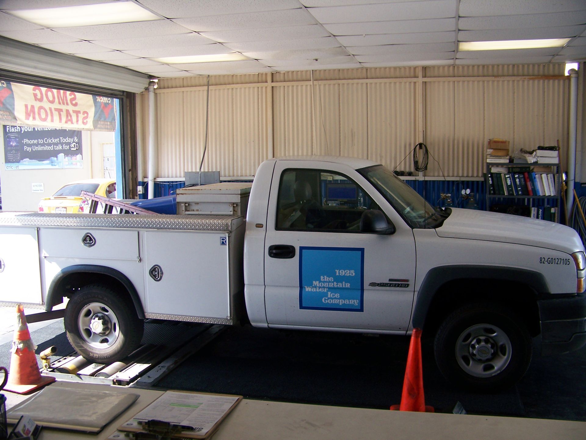 White utility pickup truck parked inside a service garage with orange cones around it
