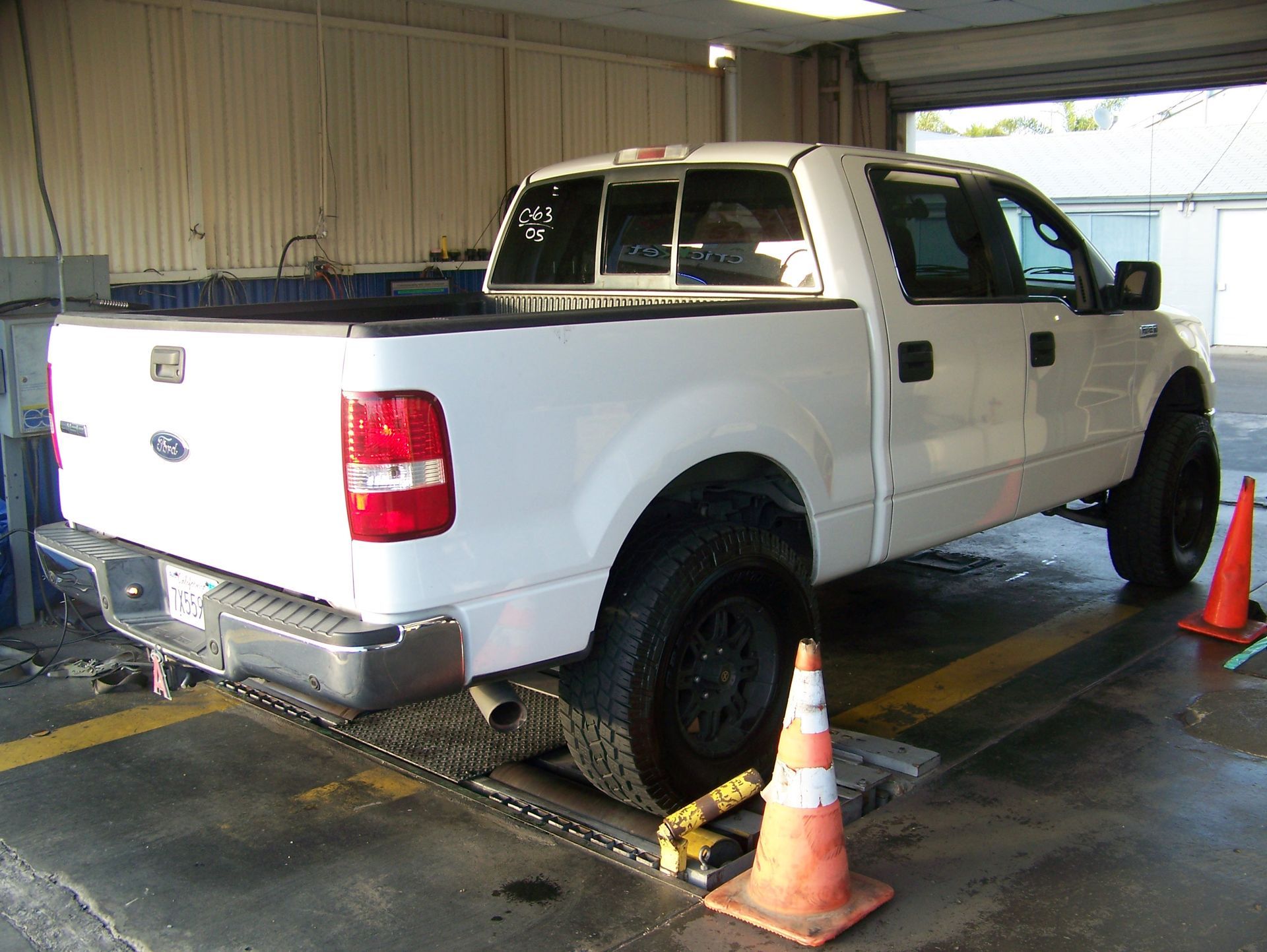White pickup truck on a car lift inside an auto shop, surrounded by traffic cones