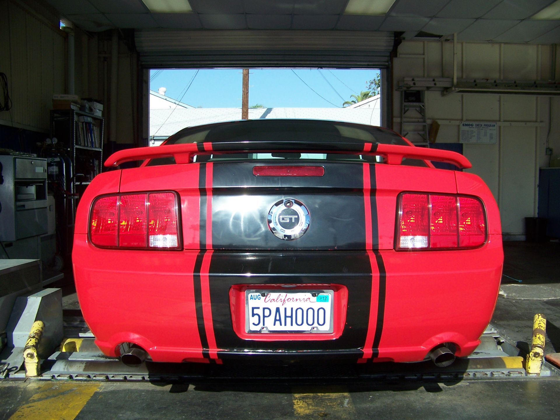 Red sports car with black racing stripes parked in a garage, rear view.