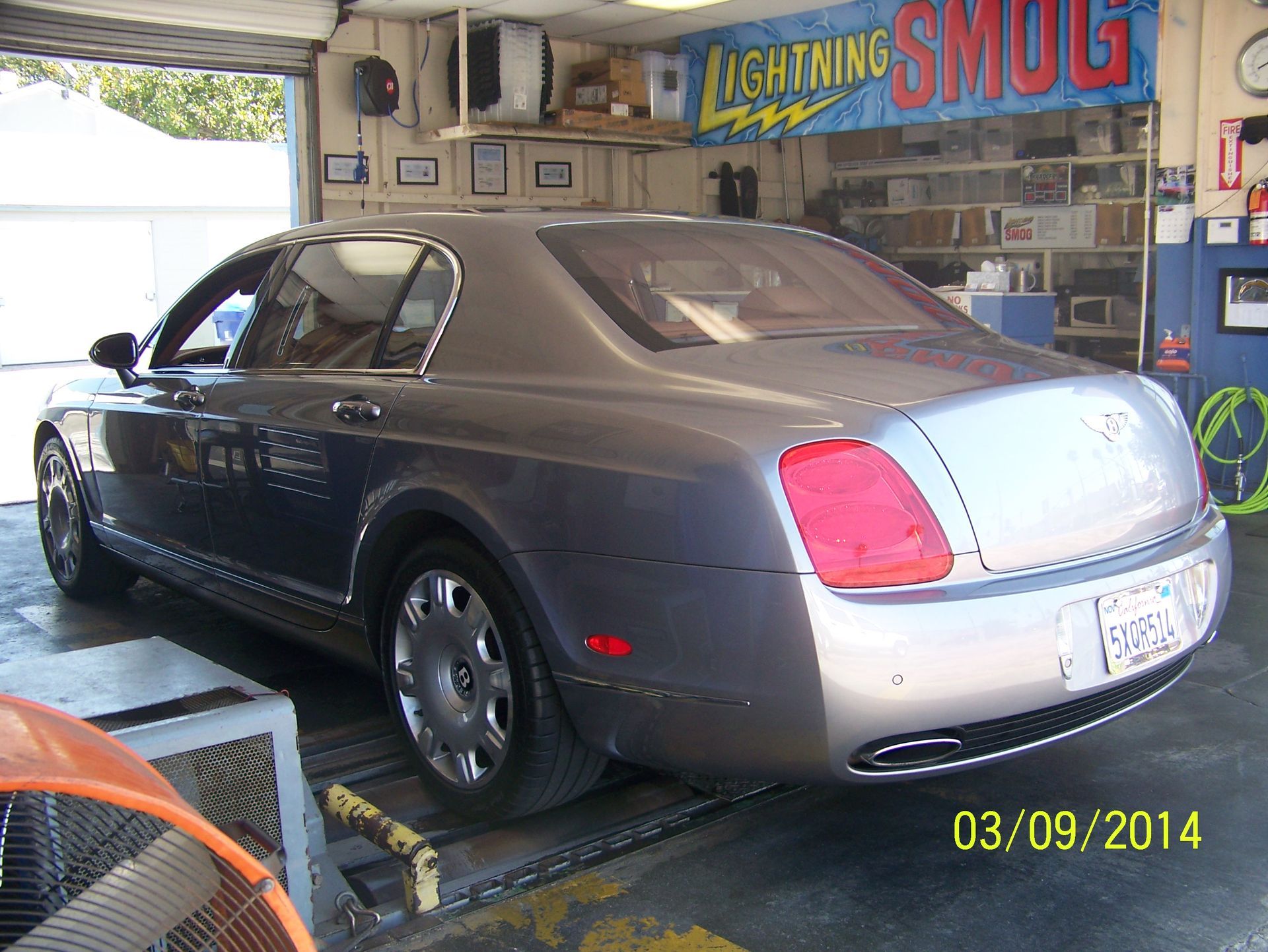 Dark gray sedan on a dyno in an auto shop garage, rear view
