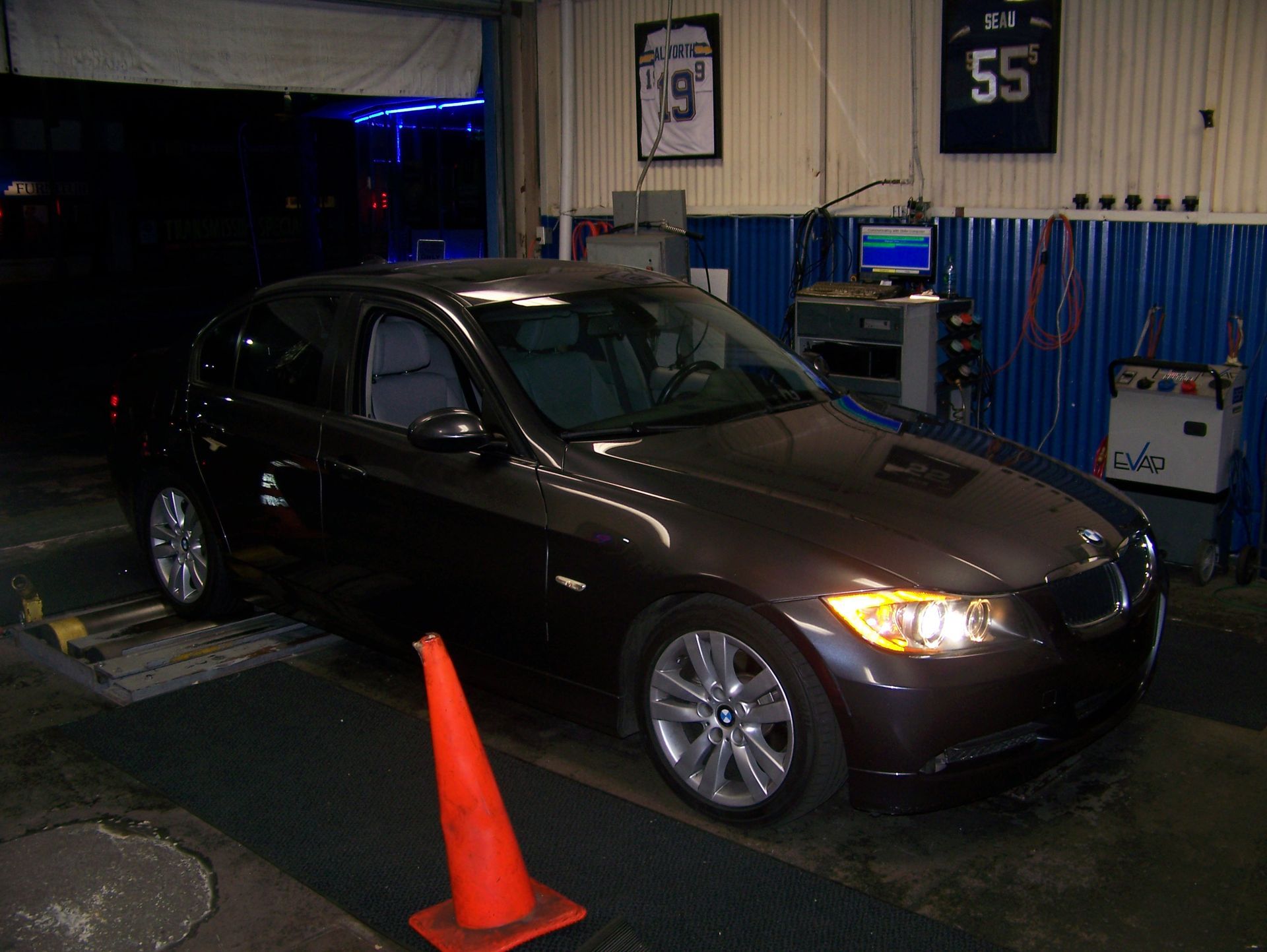 Brown sedan in a garage bay with an orange traffic cone in front of it.