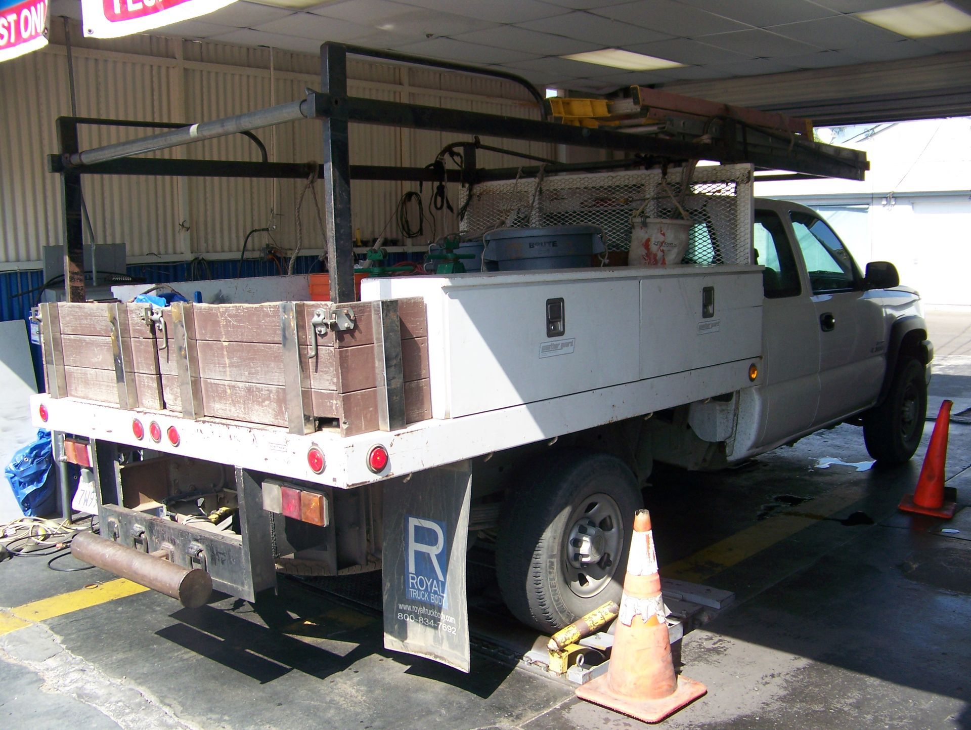 White utility pickup truck loaded with bricks, parked by a building entrance with orange cones
