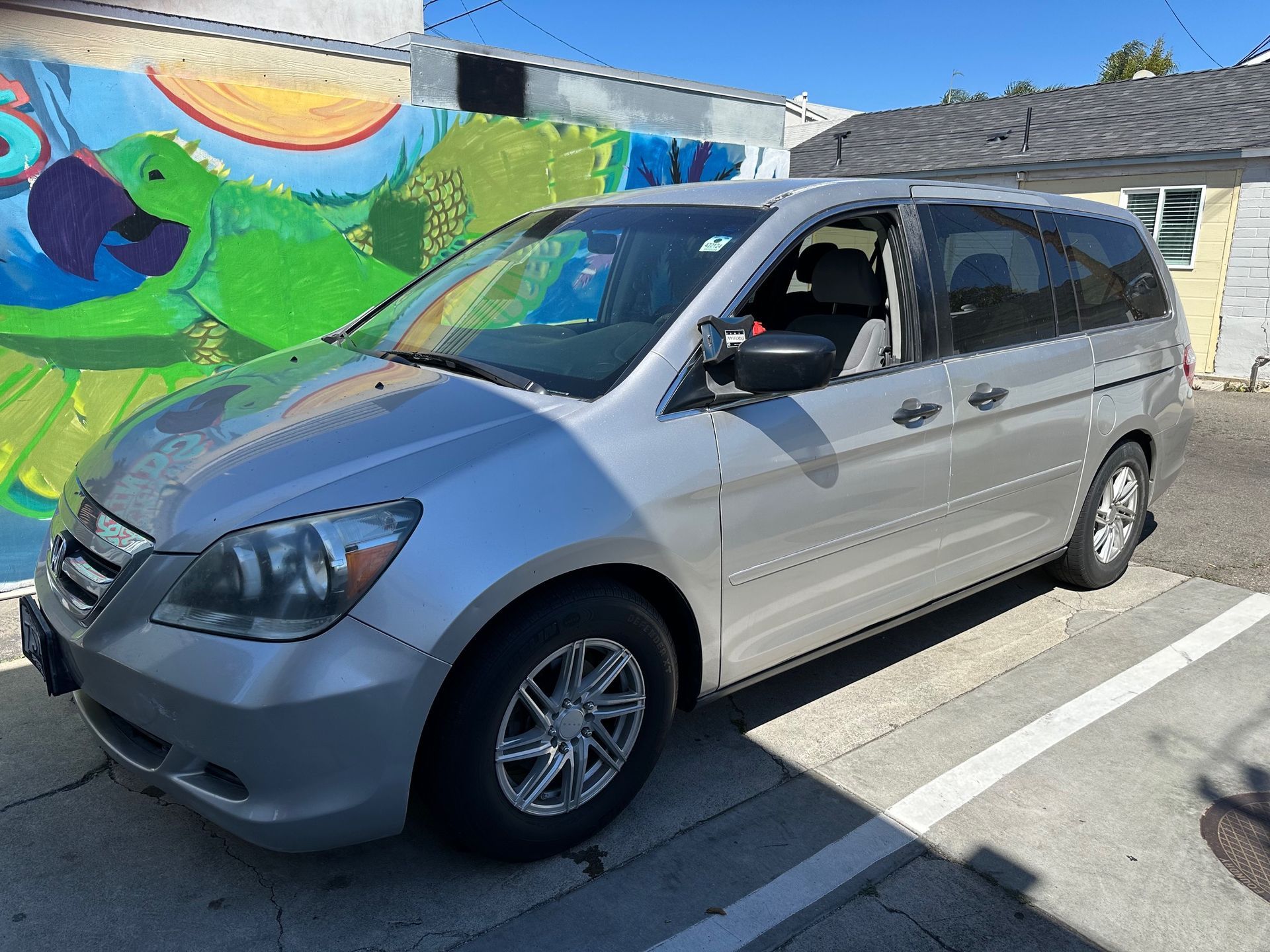 Silver minivan parked beside a colorful mural in a sunny lot