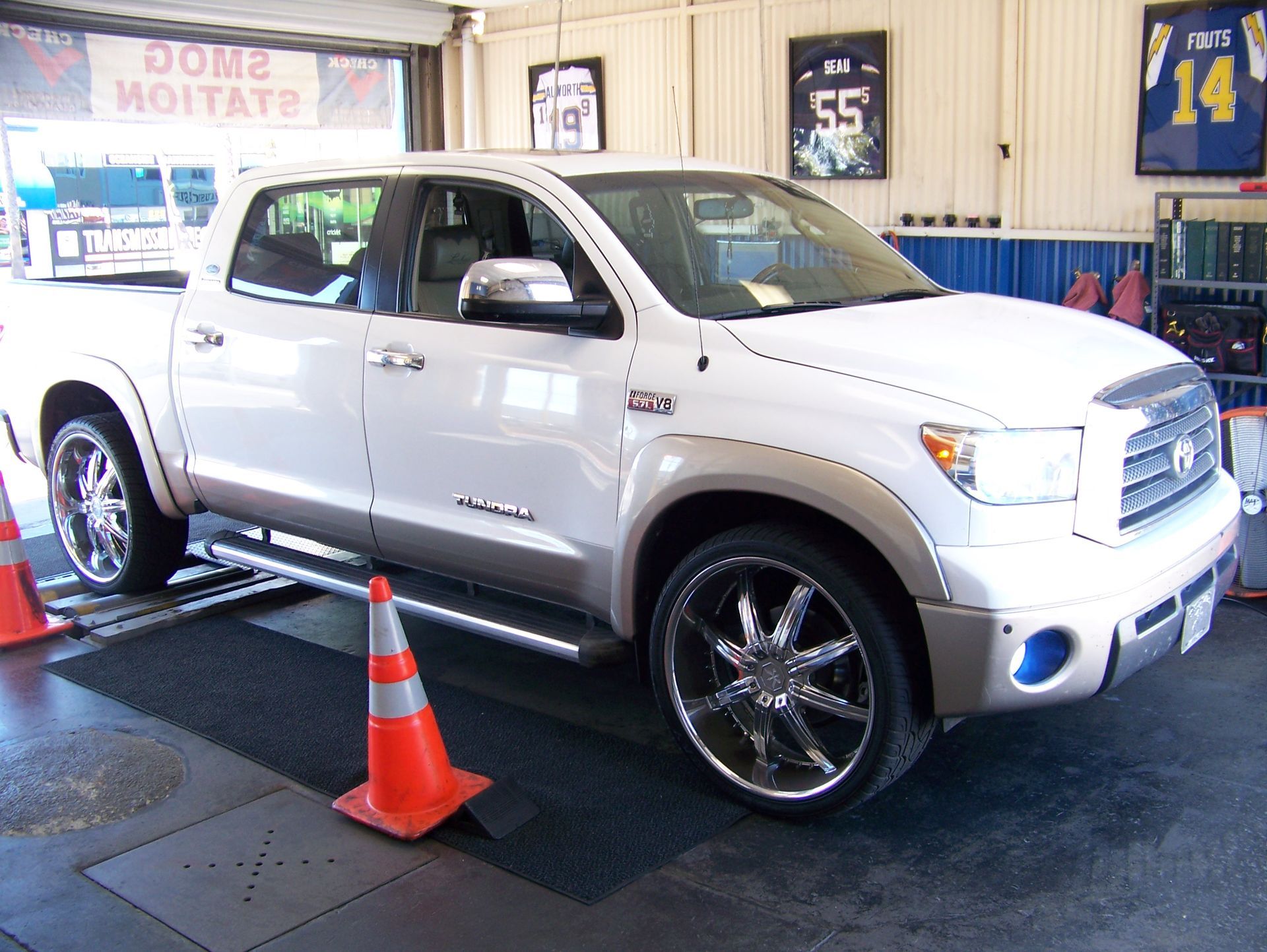 White pickup truck on a display platform indoors, with orange traffic cones and sports jerseys on the wall.